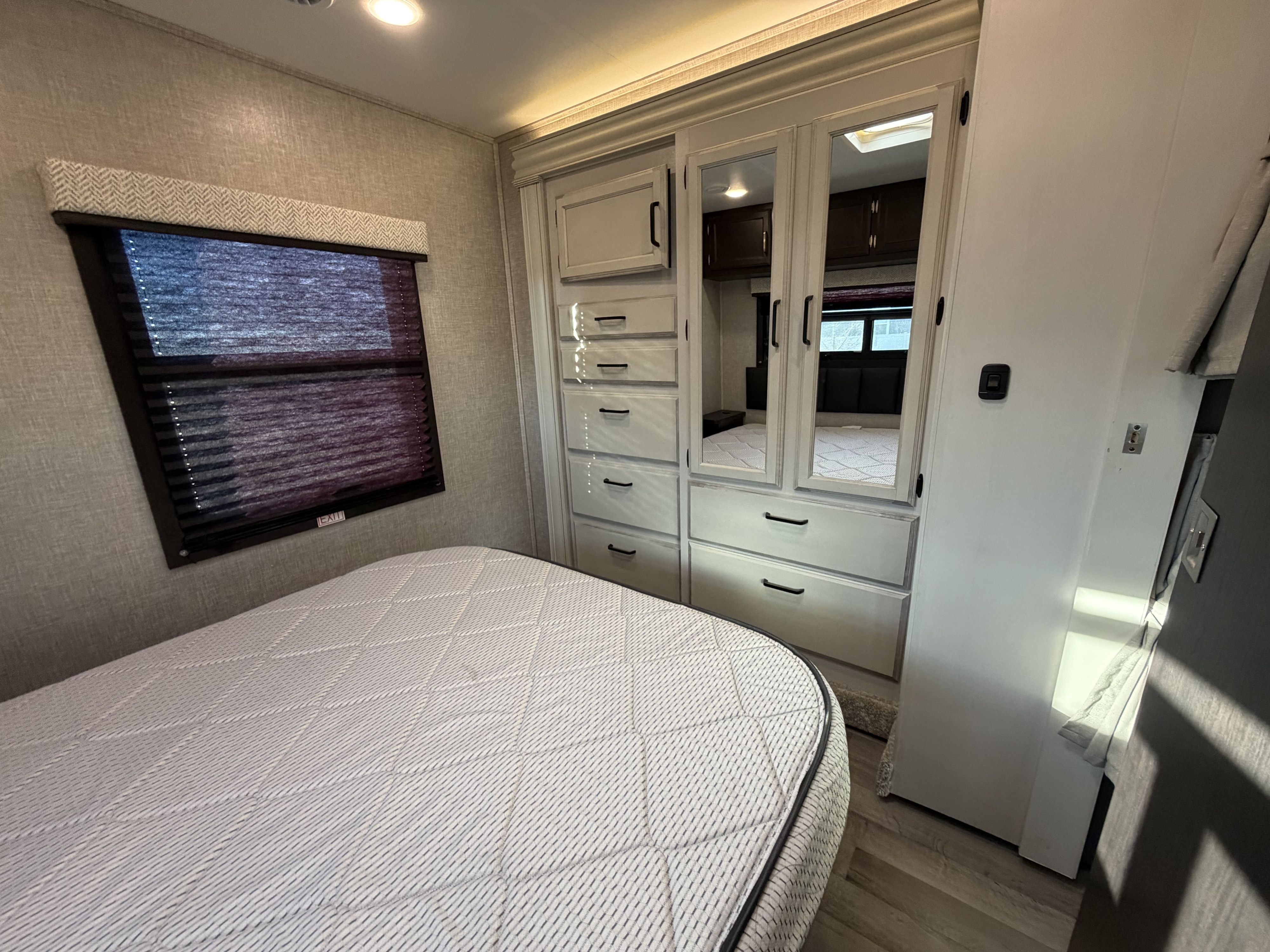Cozy rv rental bedroom with a quilted mattress, window blinds, and built-in mirrored wardrobe for organized travel stays.. Jayco Redhawk 2024