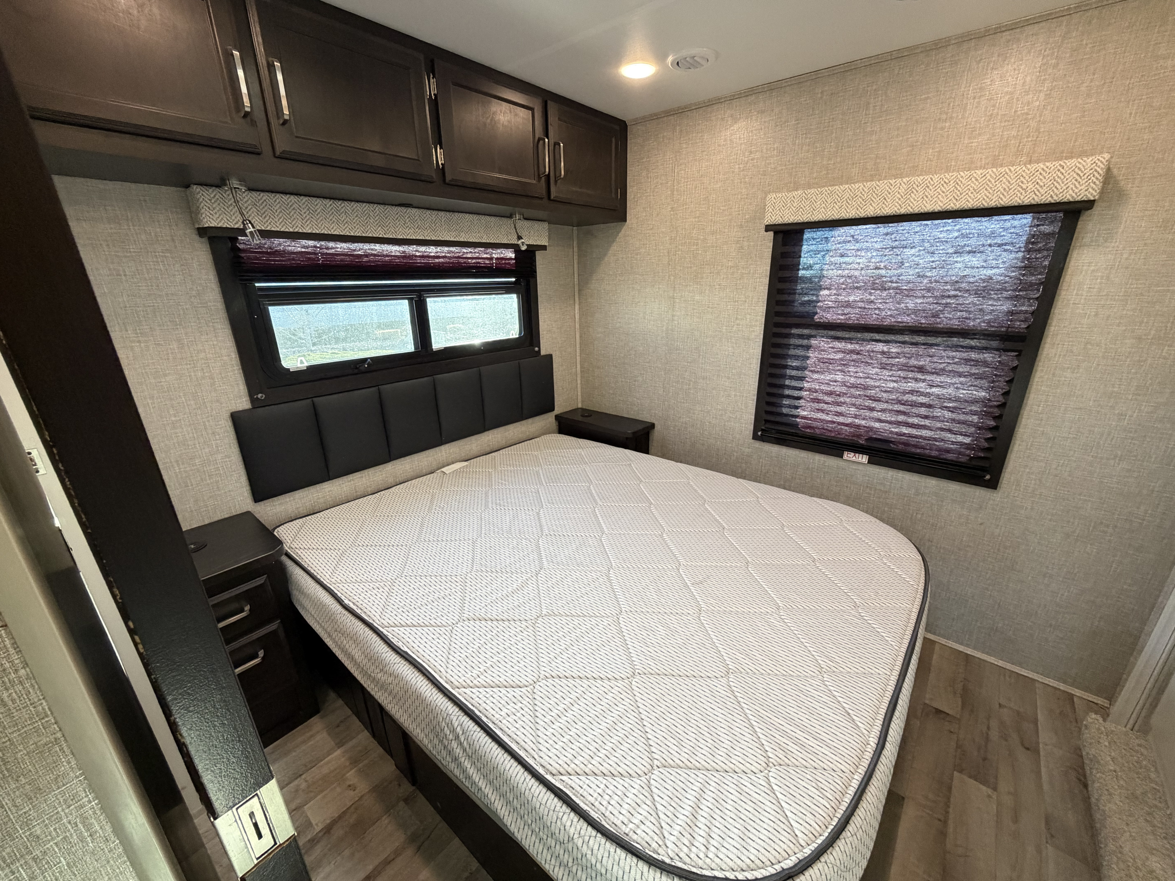 RV rental's cozy bedroom: bed with patterned mattress, dark cabinets, windows with blinds, and wood flooring.. Jayco Redhawk 2024