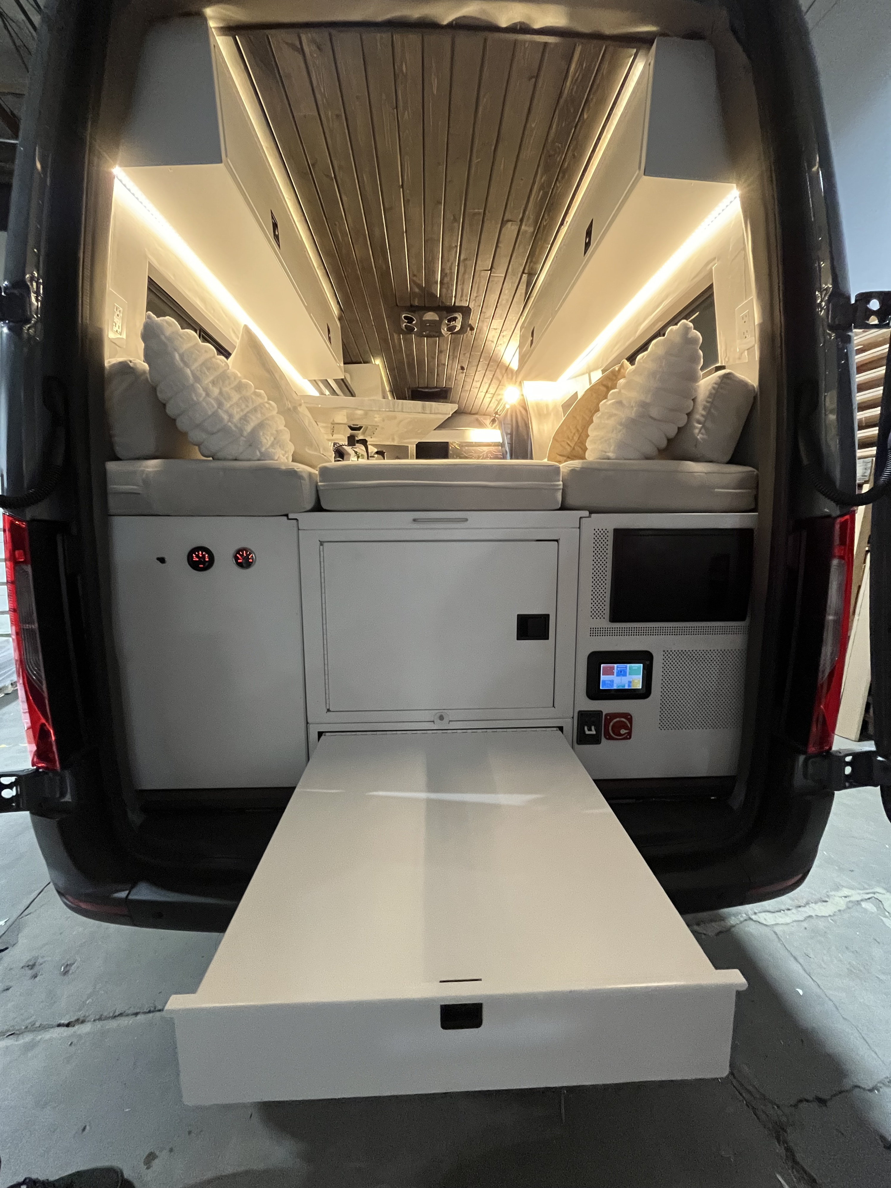 Camper van RV rental interior: A pull-out table extends, flanked by cozy seating, overhead lighting, and a wood-slat ceiling.. Mercedes-Benz Sprinter 2022
