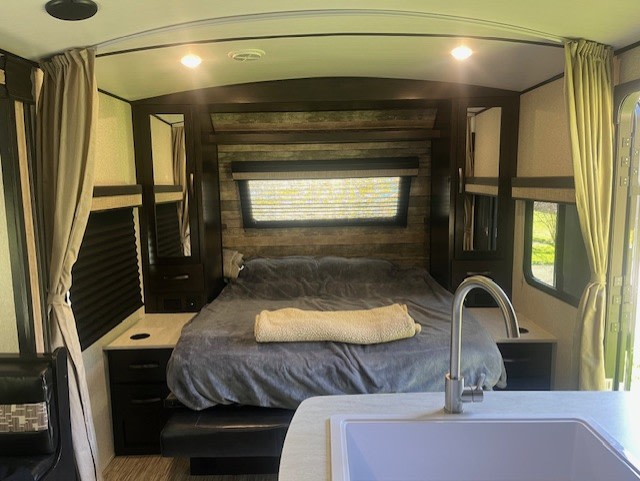 This RV rental interior showcases a cozy bedroom with a comfortable bed, windows, and a view of the kitchenette sink.. Forest River Surveyor Legend 2020