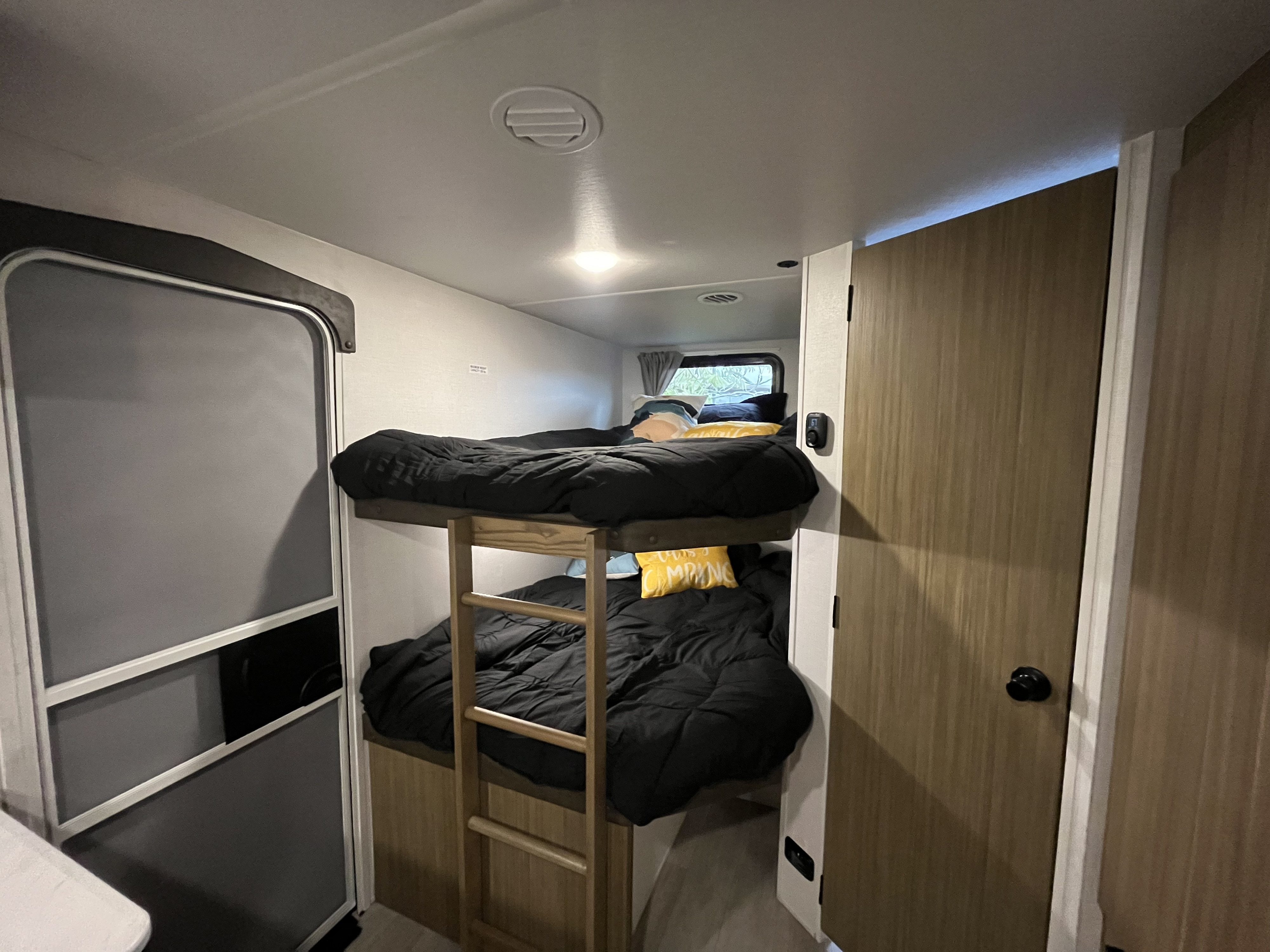 RV rental interior featuring cozy bunk beds with black comforters, a yellow camping pillow, and a wooden ladder.. Forest River EVO Lite 2025