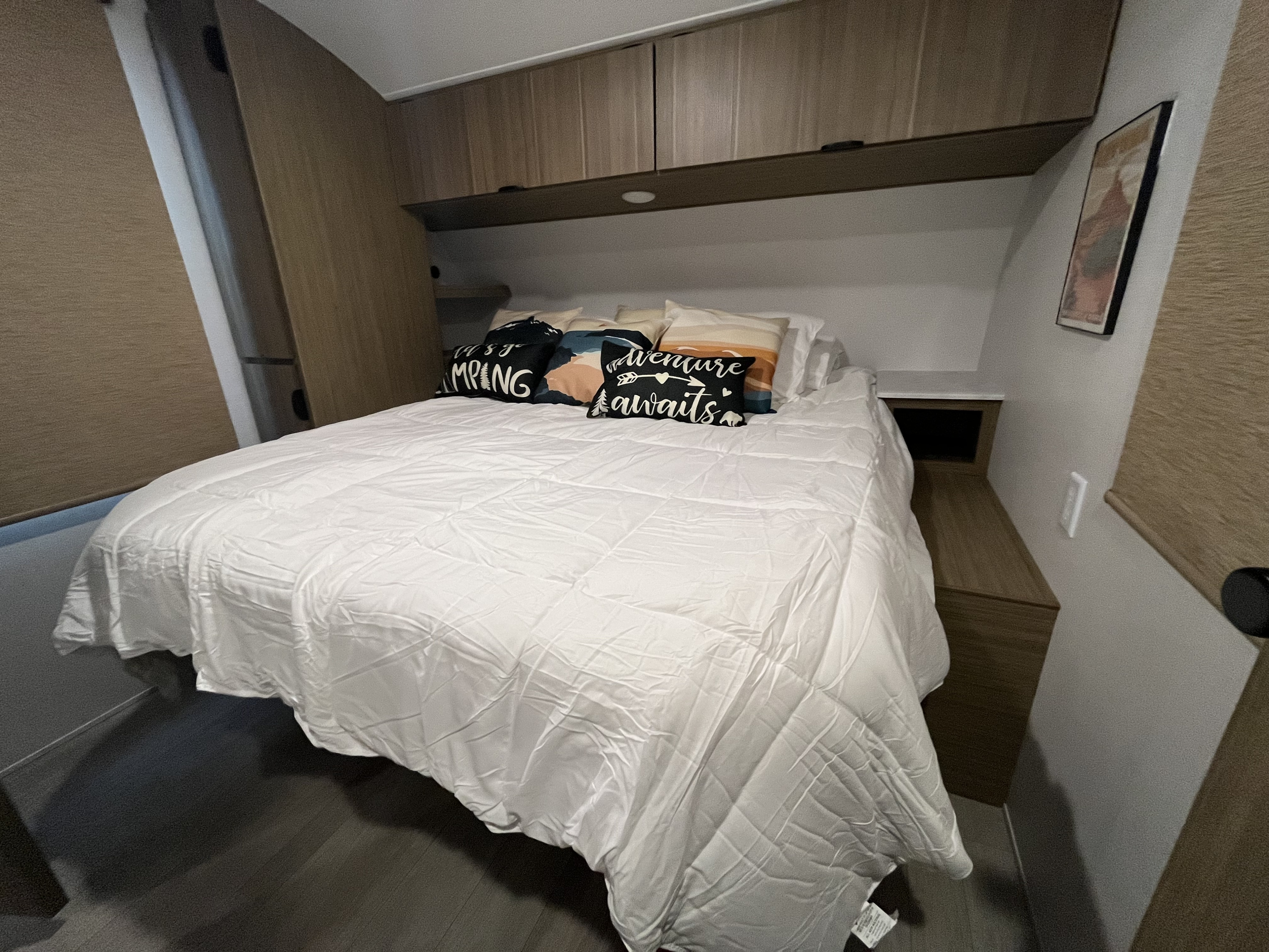 Explore this cozy RV rental bedroom. Features a comfy bed with adventure pillows, overhead storage, and a nightstand.. Forest River EVO Lite 2025