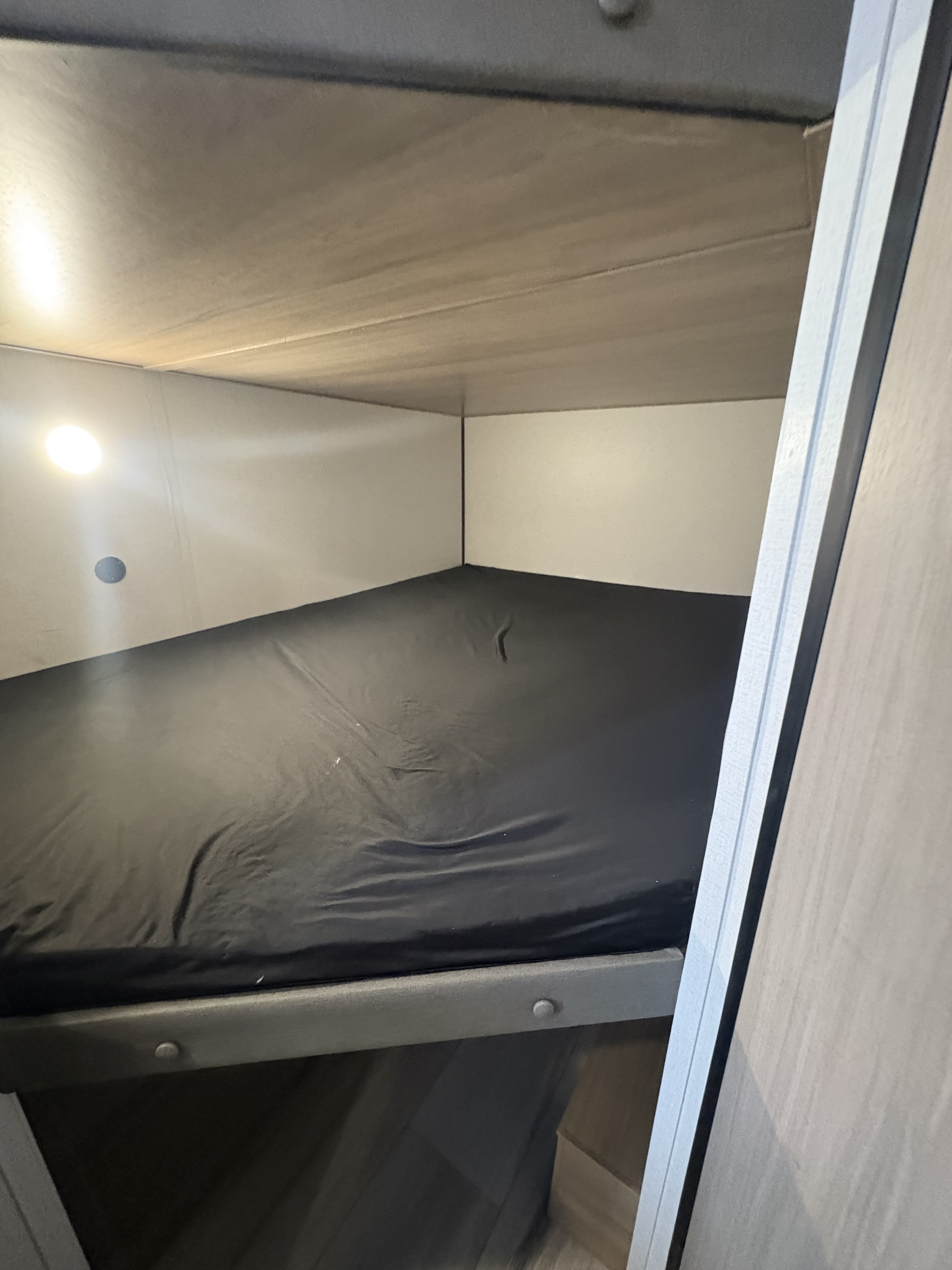 Inside an RV rental: a compact bunk bed with black fitted sheets and an overhead light, perfect for comfortable sleeping.. Keystone RV Coleman 2025