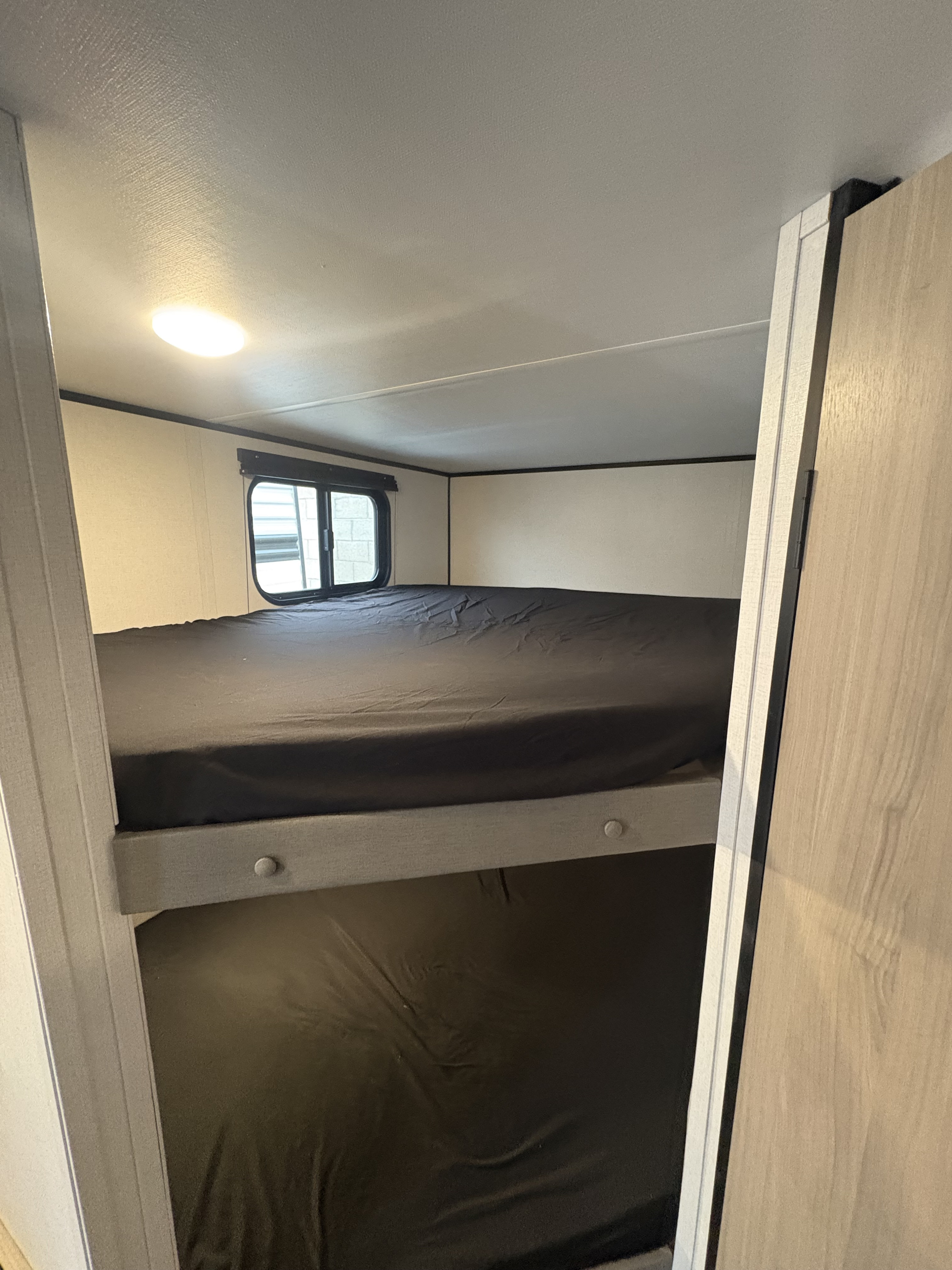 Inside an RV rental: View of upper and lower bunk beds with dark bedding, a window, and a ceiling light.. Keystone RV Coleman 2025