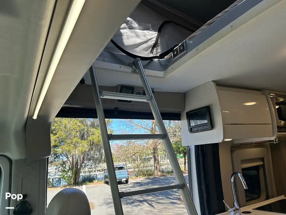 RV rental: Interior view with a ladder to the pop-top bunk, display screen, partial kitchen, and an exterior view of trees and water.. Thor Tellaro 2023