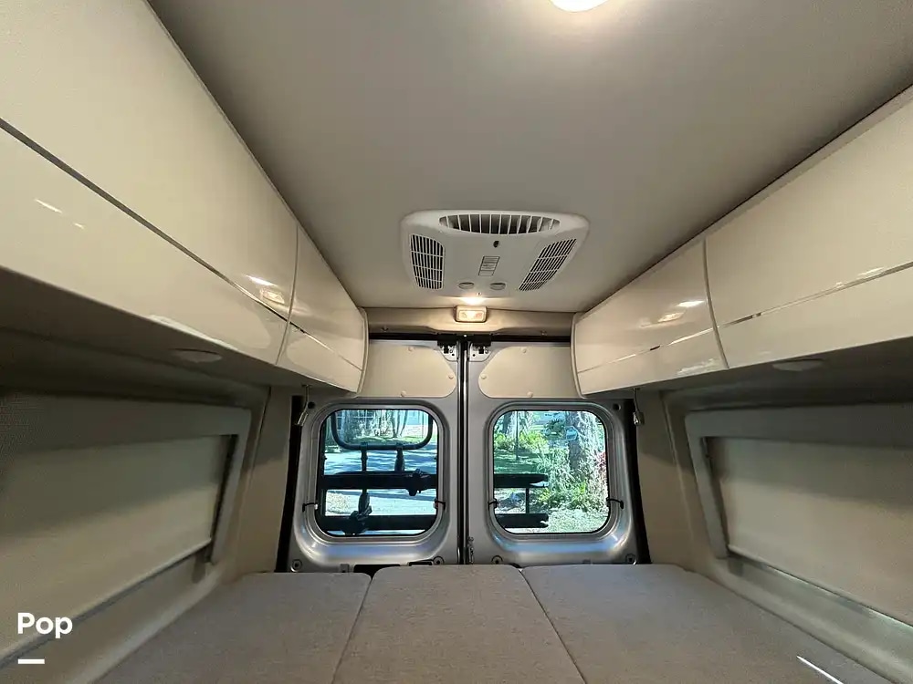 Inside your cozy rv rental: rear bedroom area with comfortable bed, overhead cabinets, and clear views from the back windows.. Thor Tellaro 2023