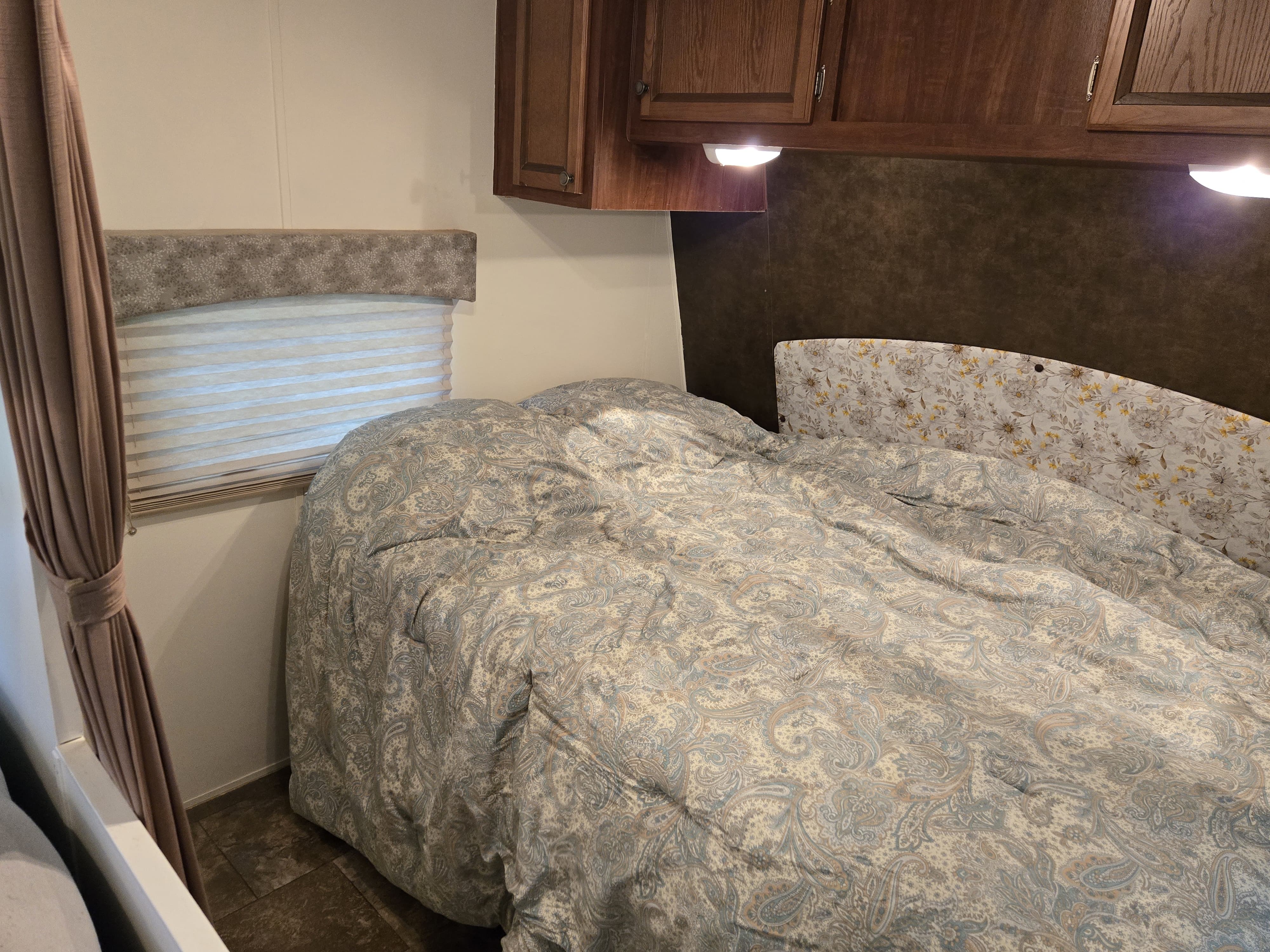 Snug RV rental bedroom with a bed, paisley comforter, floral headboard, wood cabinets, and window.. Jayco Jay Flight 2013