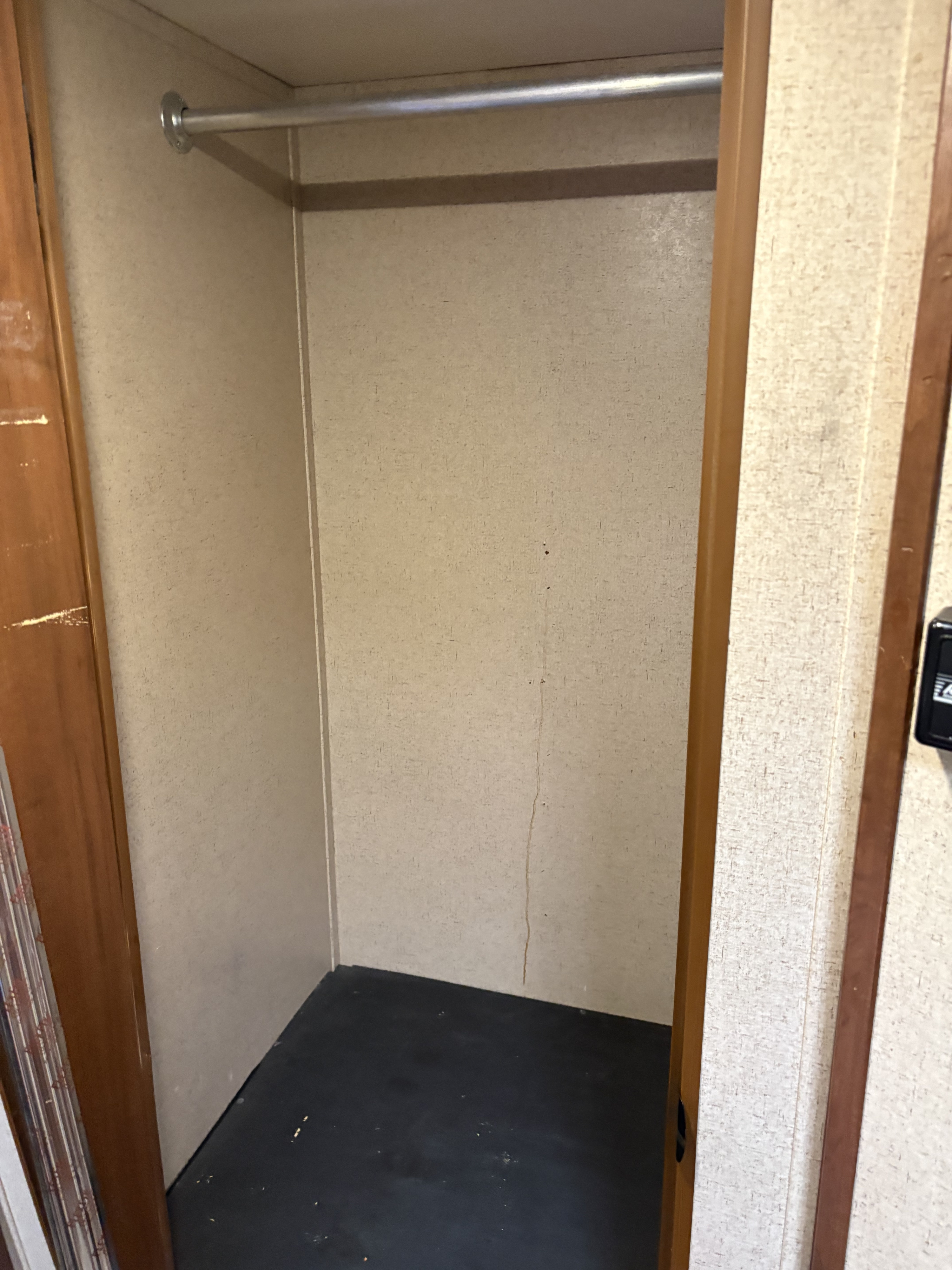 Empty RV rental closet features a clothes rod, textured beige walls, dark floor, and light wood trim. Note the faint wall stain.. Jayco Jay Flight 2016