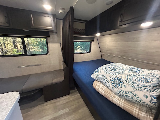 Cozy RV rental interior featuring a comfortable bed, dinette, overhead storage, and scenic window views of nature.. Jayco Jay Flight SLX 2022