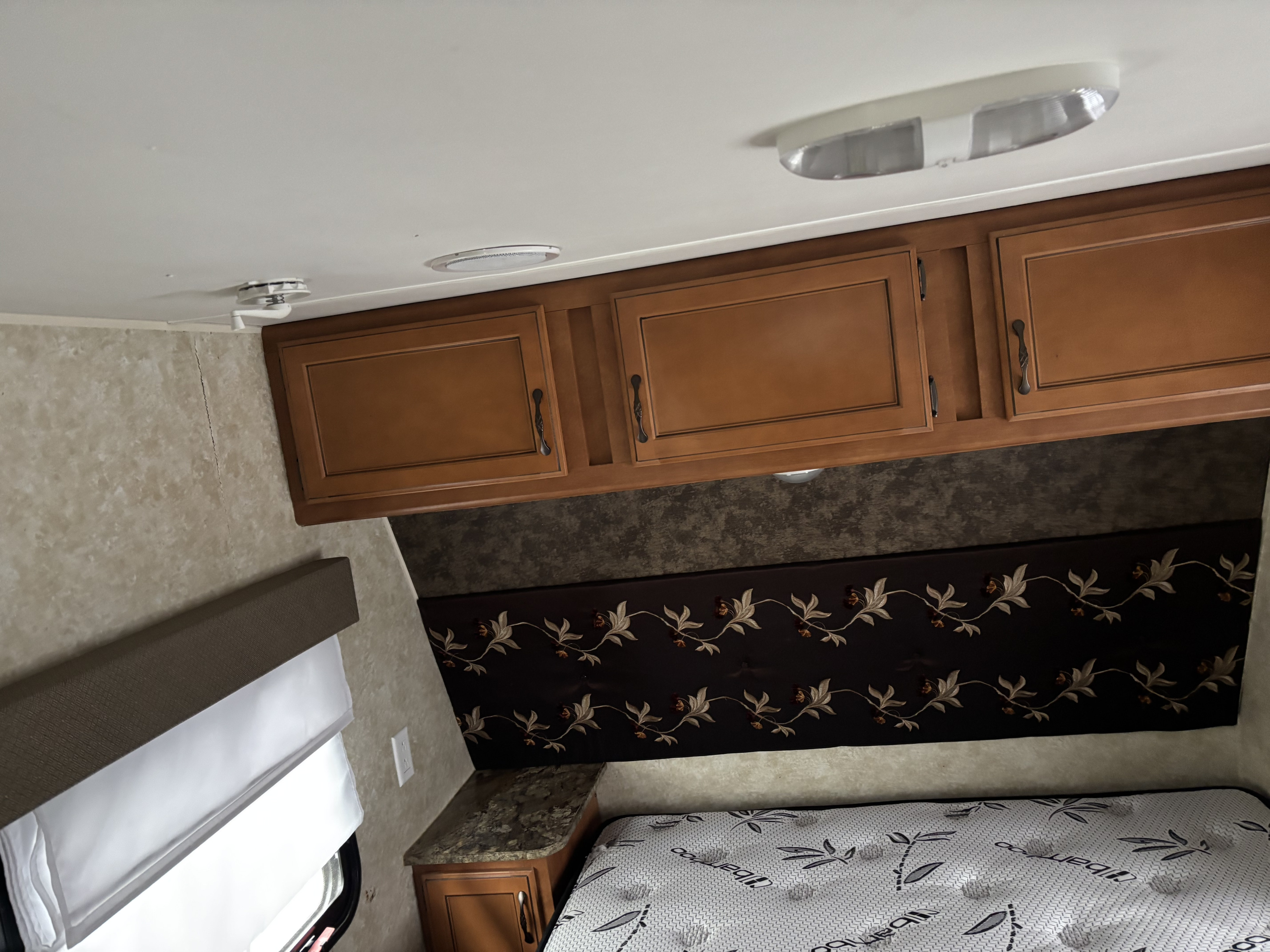 Cozy RV rental bedroom featuring wood cabinets, a "Bamboo" mattress, decorative wall, and a window.. Gulf Stream Kingsport 2015