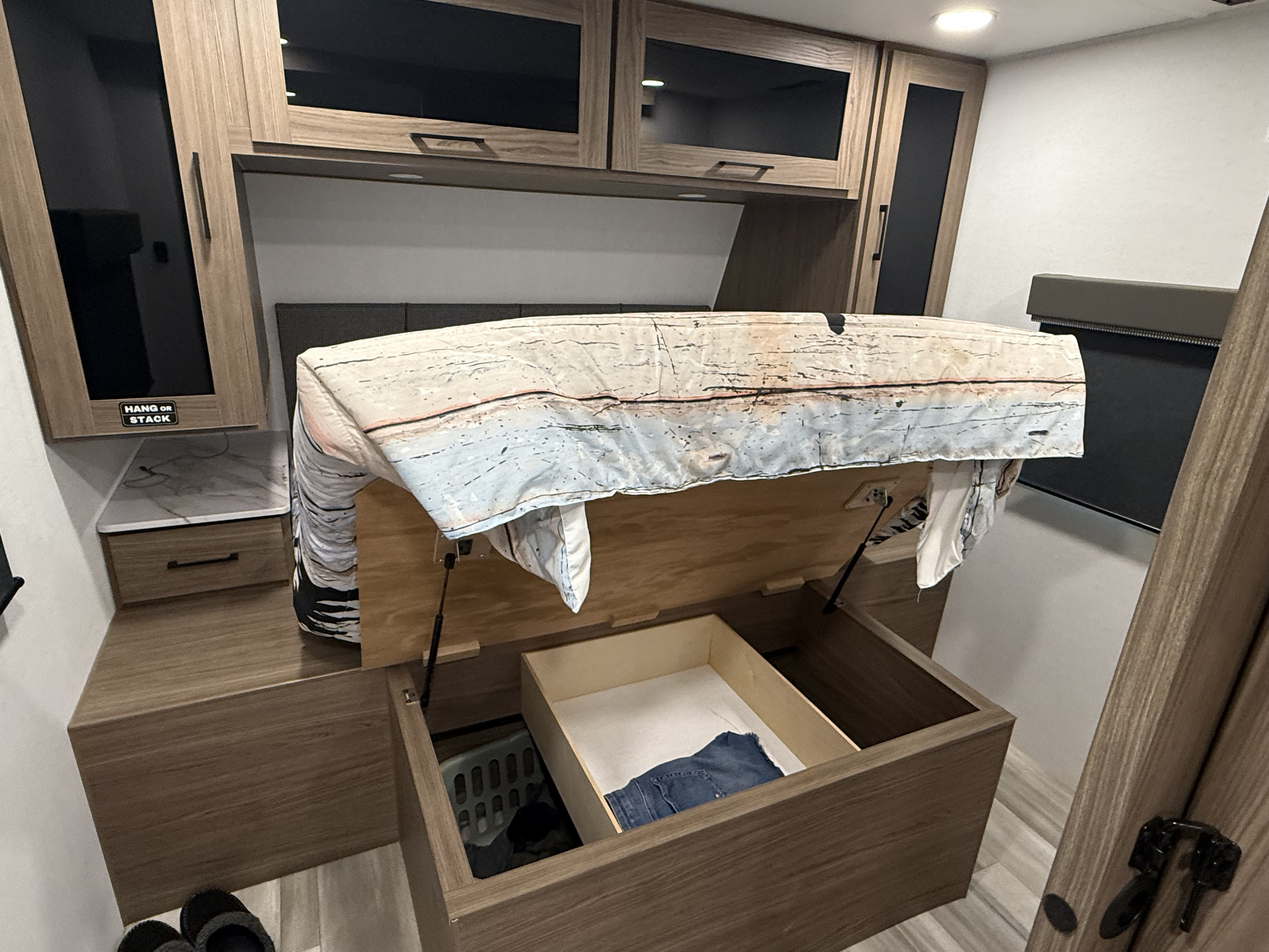 Inside an **rv rental**: view of a bedroom with a raised bed revealing spacious storage, including a laundry hamper and clothes drawer.. Alliance RV Delta Ultra Light 2025