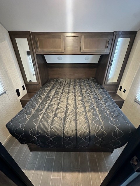 Spacious RV rental bedroom with a large bed, dark comforter, overhead storage, side mirrors, and wood-look flooring.. Forest River Cherokee Grey Wolf 2020