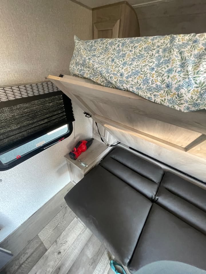 Cozy RV rental interior with a bunk bed featuring floral bedding, comfortable seating, and a window with blinds.. KZ Escape 2022