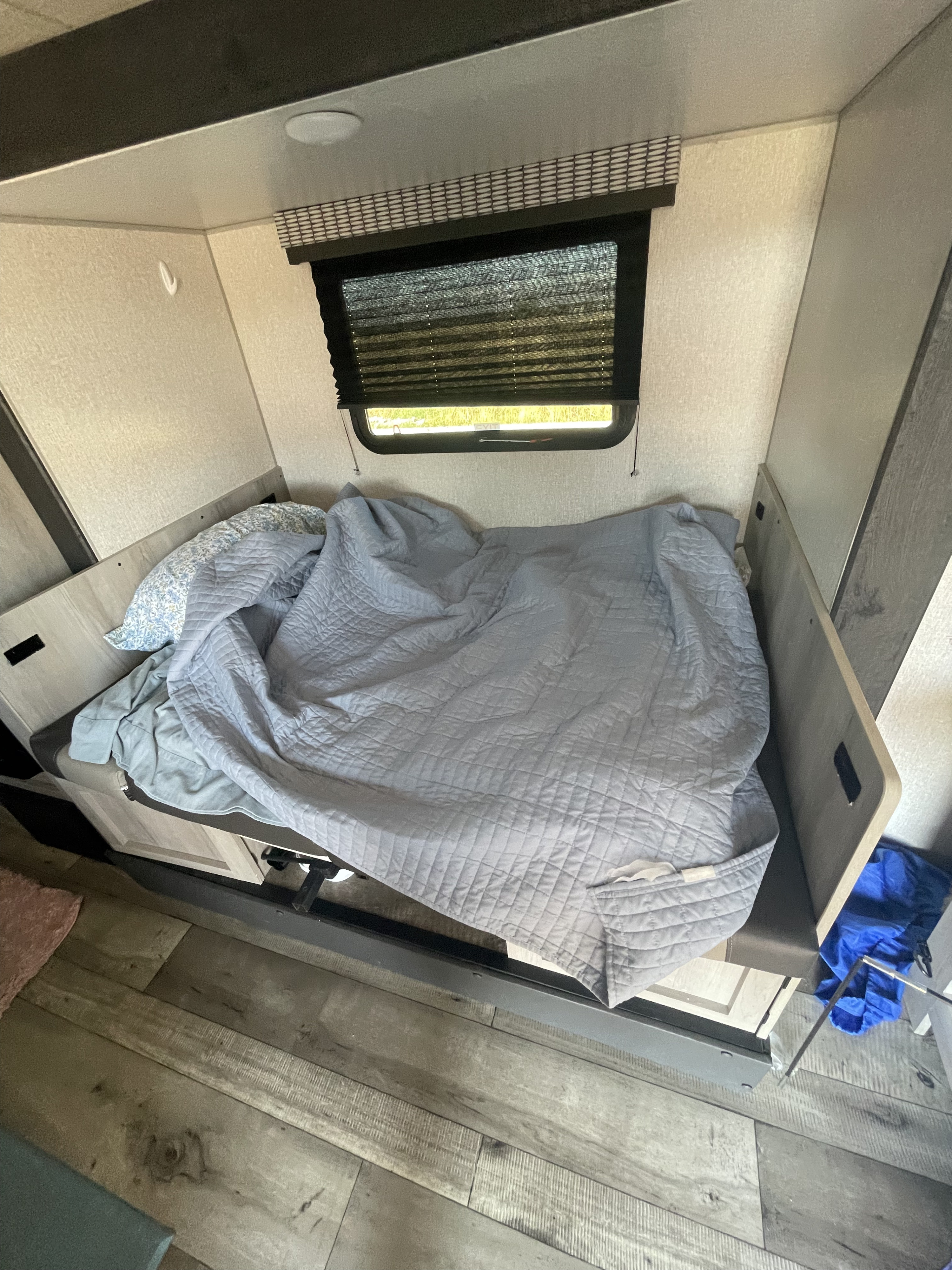 RV rental's cozy sleeping area features a made bed with a gray quilted blanket, a floral pillow, and a window with blinds.. KZ Escape 2022