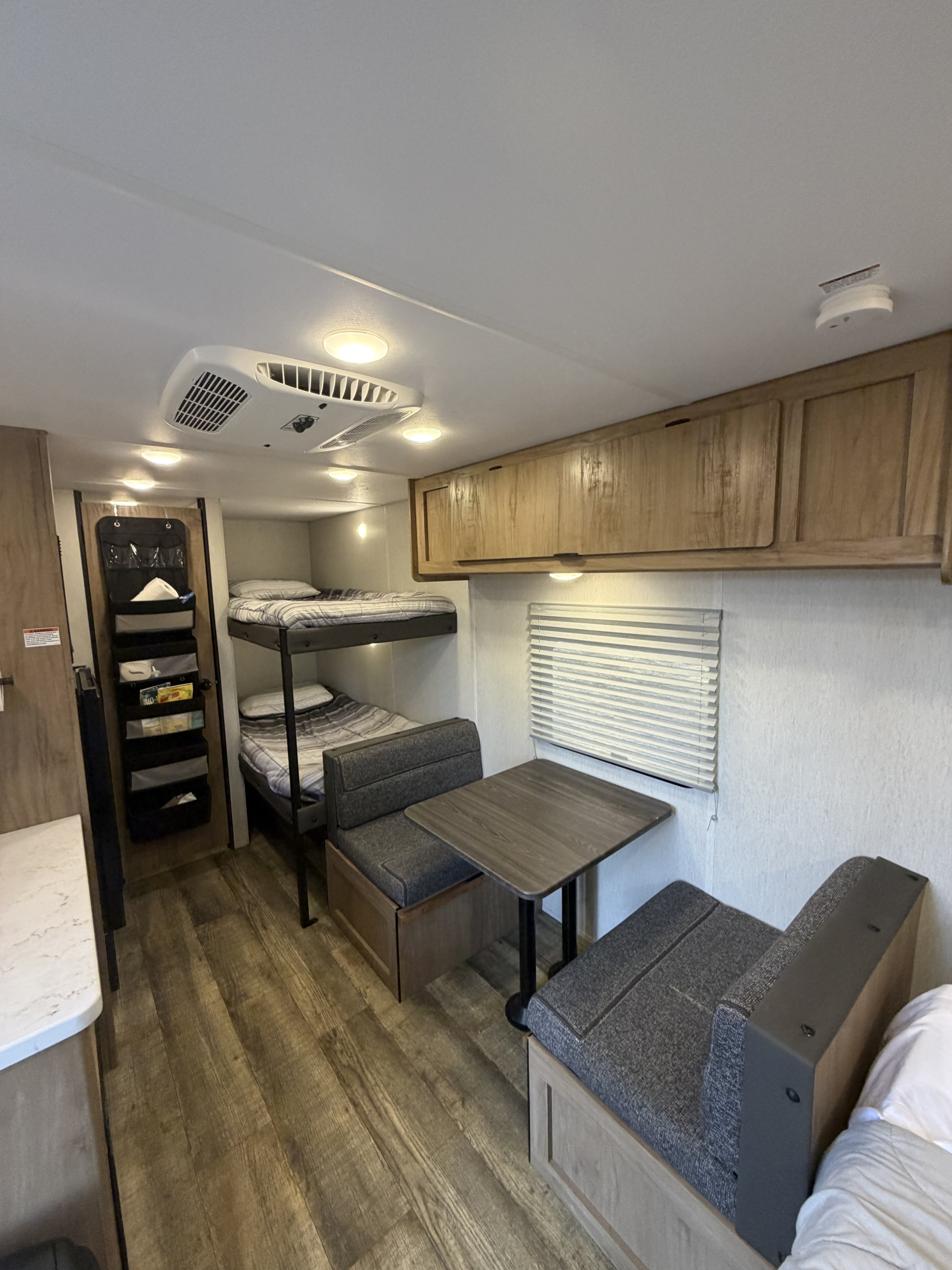 RV rental interior showing bunk beds, a dinette with table & benches, overhead cabinets, and wood-look flooring.. Forest River Cherokee Wolf Den 2024