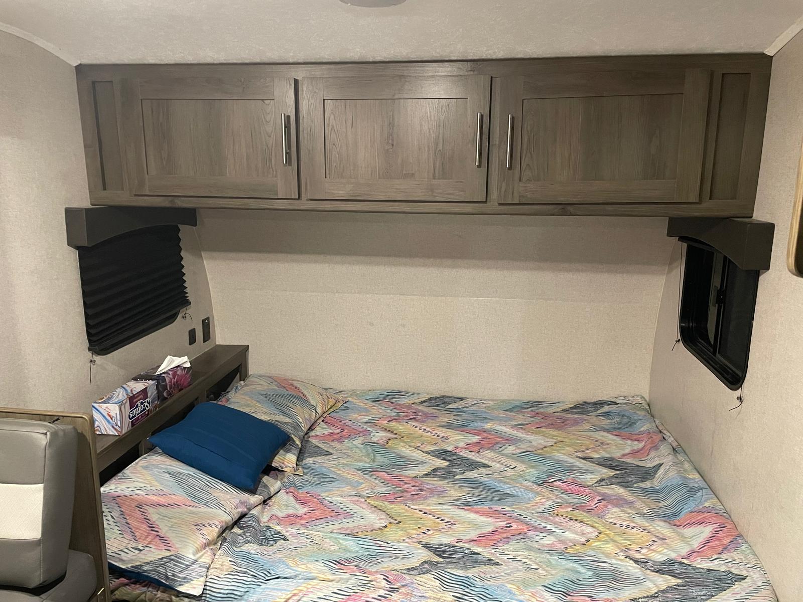 RV rental bedroom with patterned bed, wood cabinets, and window offers cozy accommodations.. Coachmen Viking 17BHS 2021