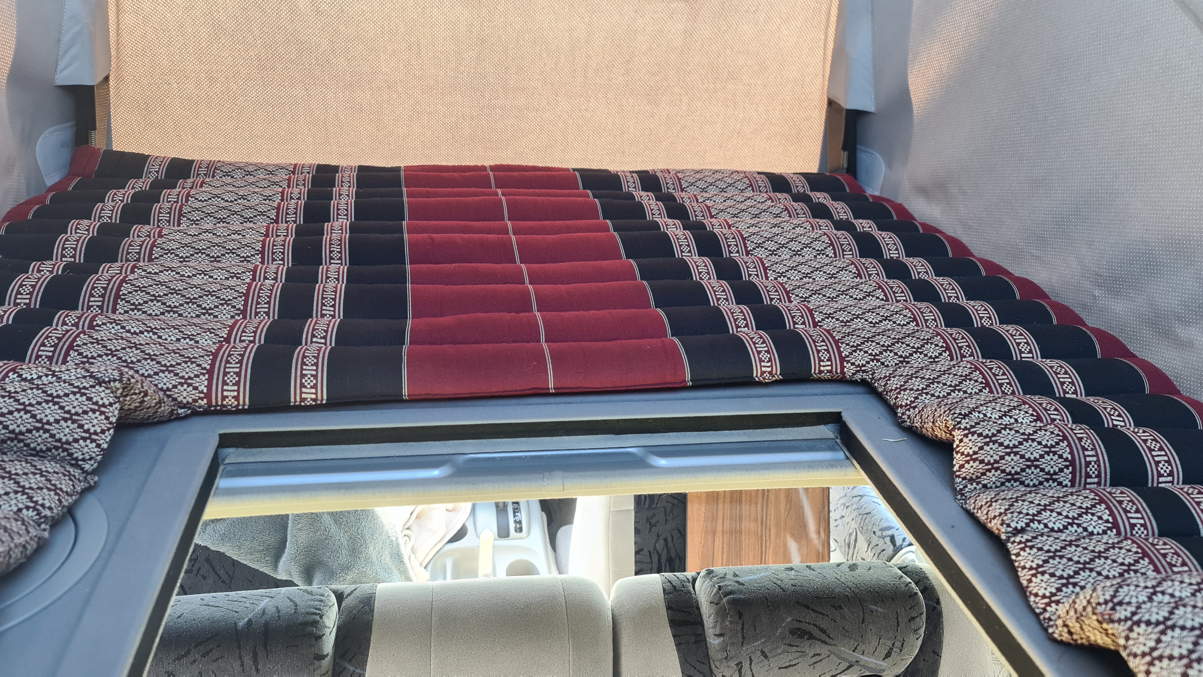 Cozy, patterned sleeping mat in an RV rental, positioned over back seats, offering comfy rest space.. Mazda Bongo 2002