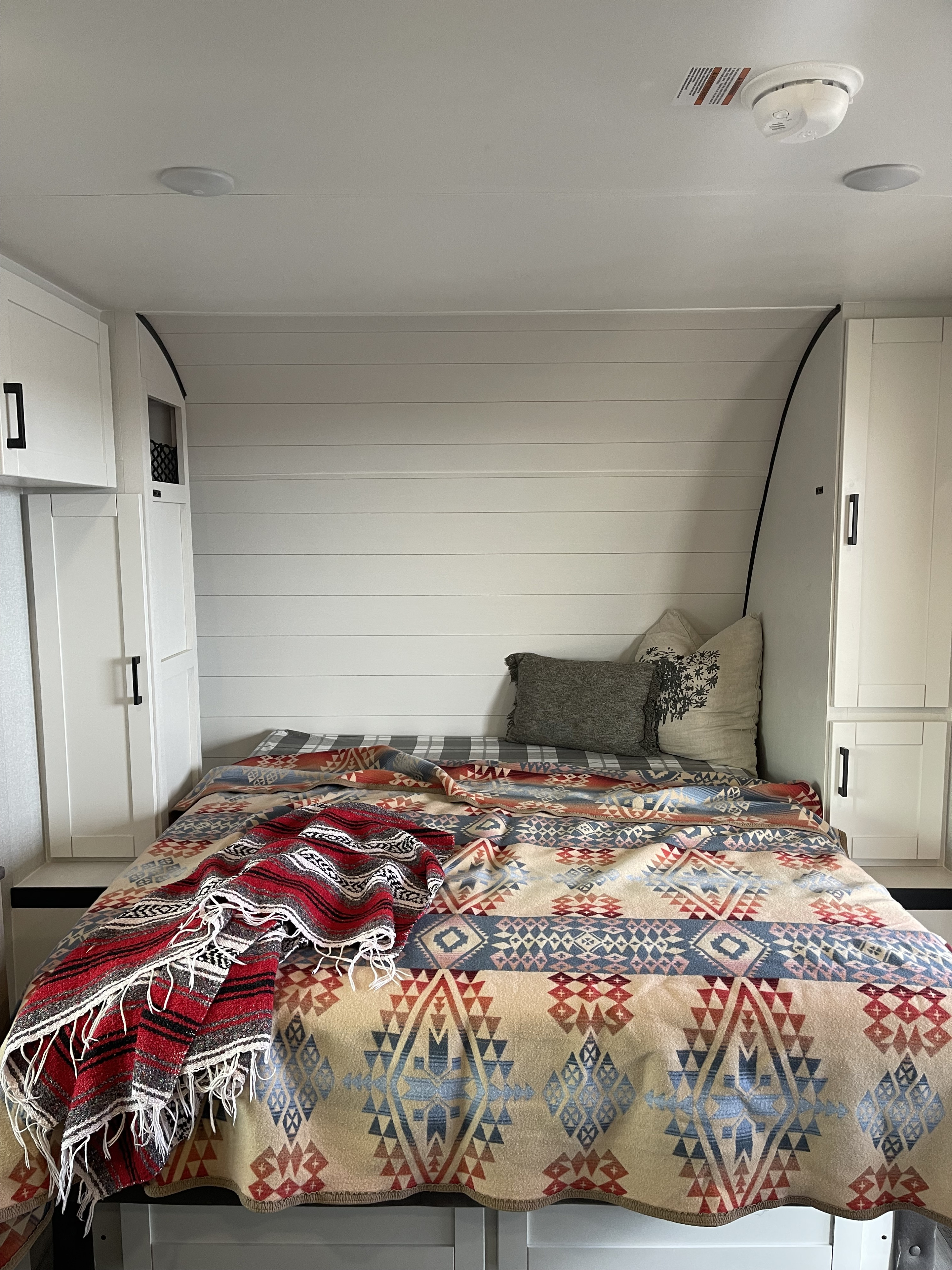 Colorful blankets on a bed in a cozy RV rental bedroom with white shiplap walls and built-in storage.. Jayco 197 MBW Baja 2026