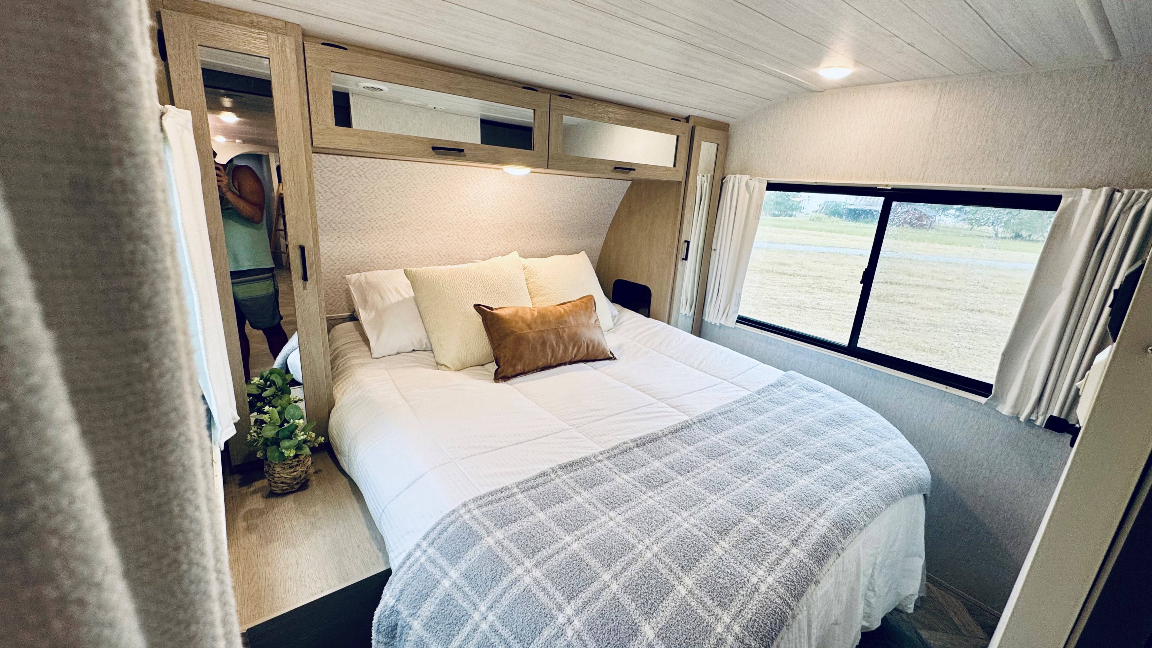 Step into this inviting RV rental bedroom featuring a comfy bed, overhead storage, and a window with outdoor views.. Forest River Salem Platinum 2024