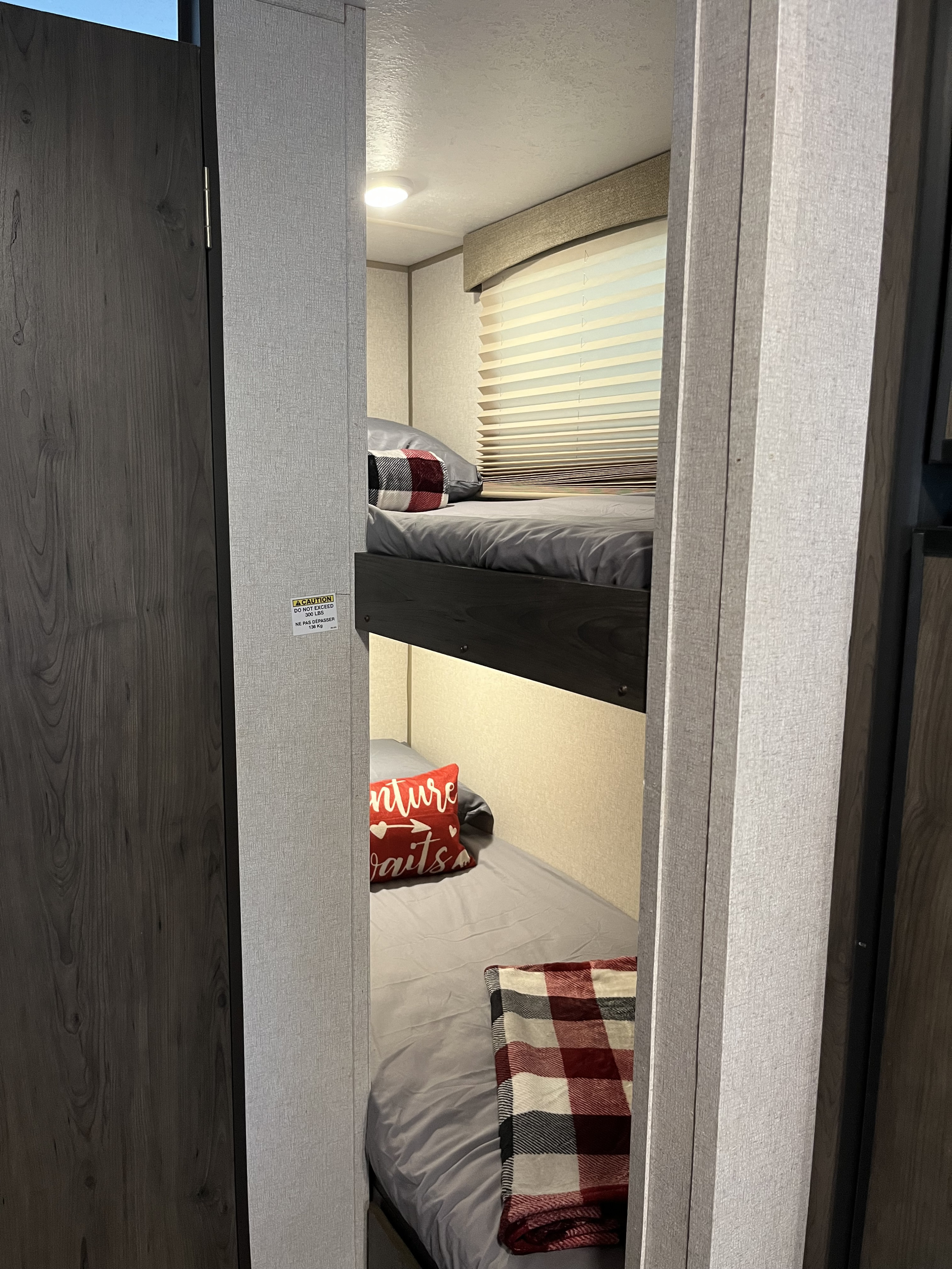 Inside an RV rental: clean, cozy bunk beds with plaid blankets & window blinds. A 300 lb weight limit is visible.. Coachmen Viking Saga 21SBH 2019
