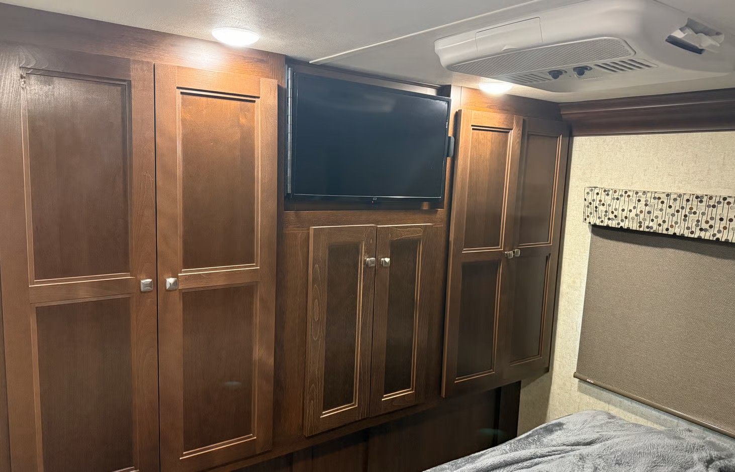 RV rental bedroom with sleek wooden cabinets, a wall-mounted TV, and an overhead AC unit, providing comfort and storage.. Forest River Sunseeker 2019