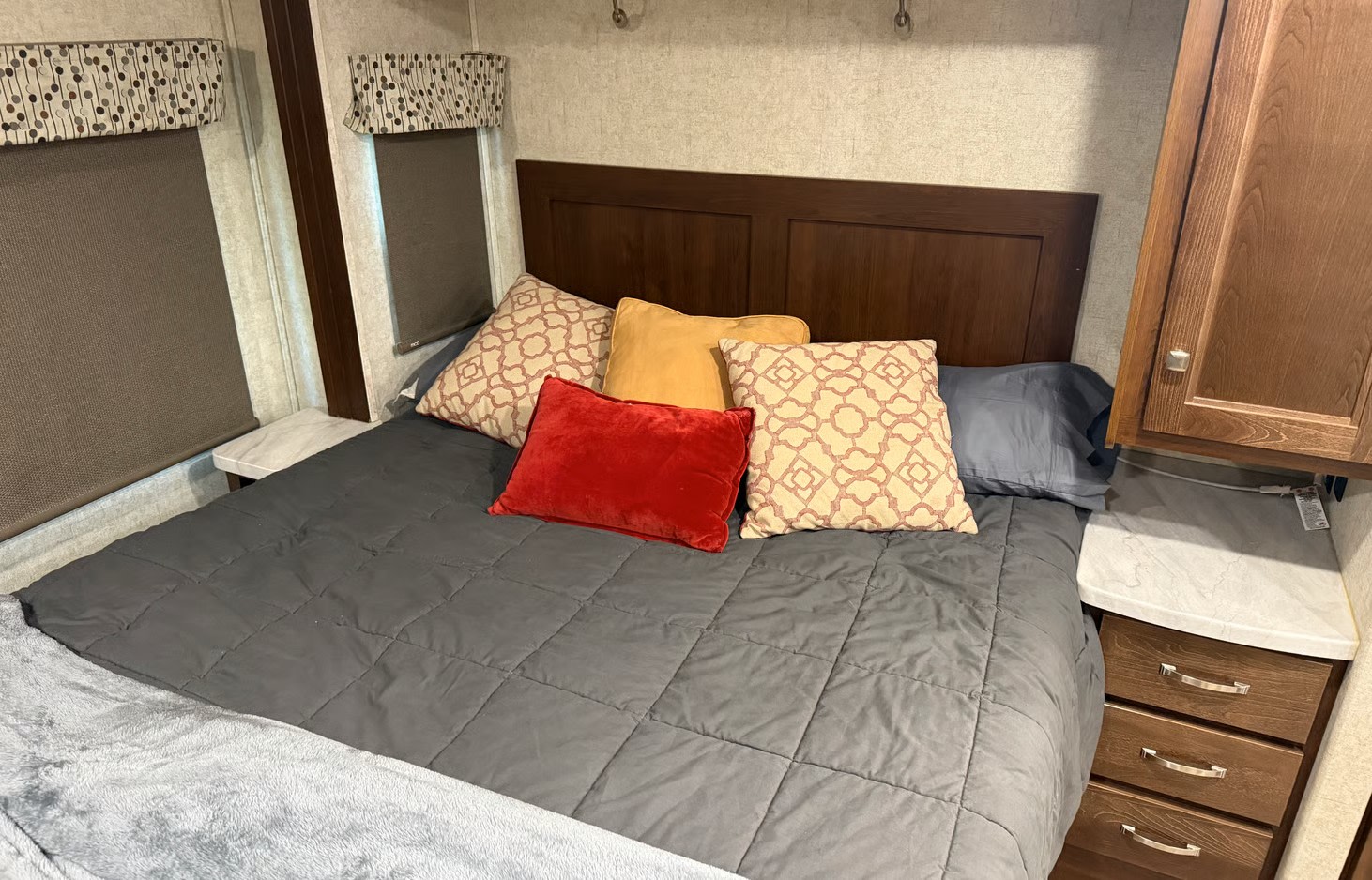 Cozy RV rental bedroom with a comfy bed, colorful pillows, a wooden headboard, and compact storage.. Forest River Sunseeker 2019