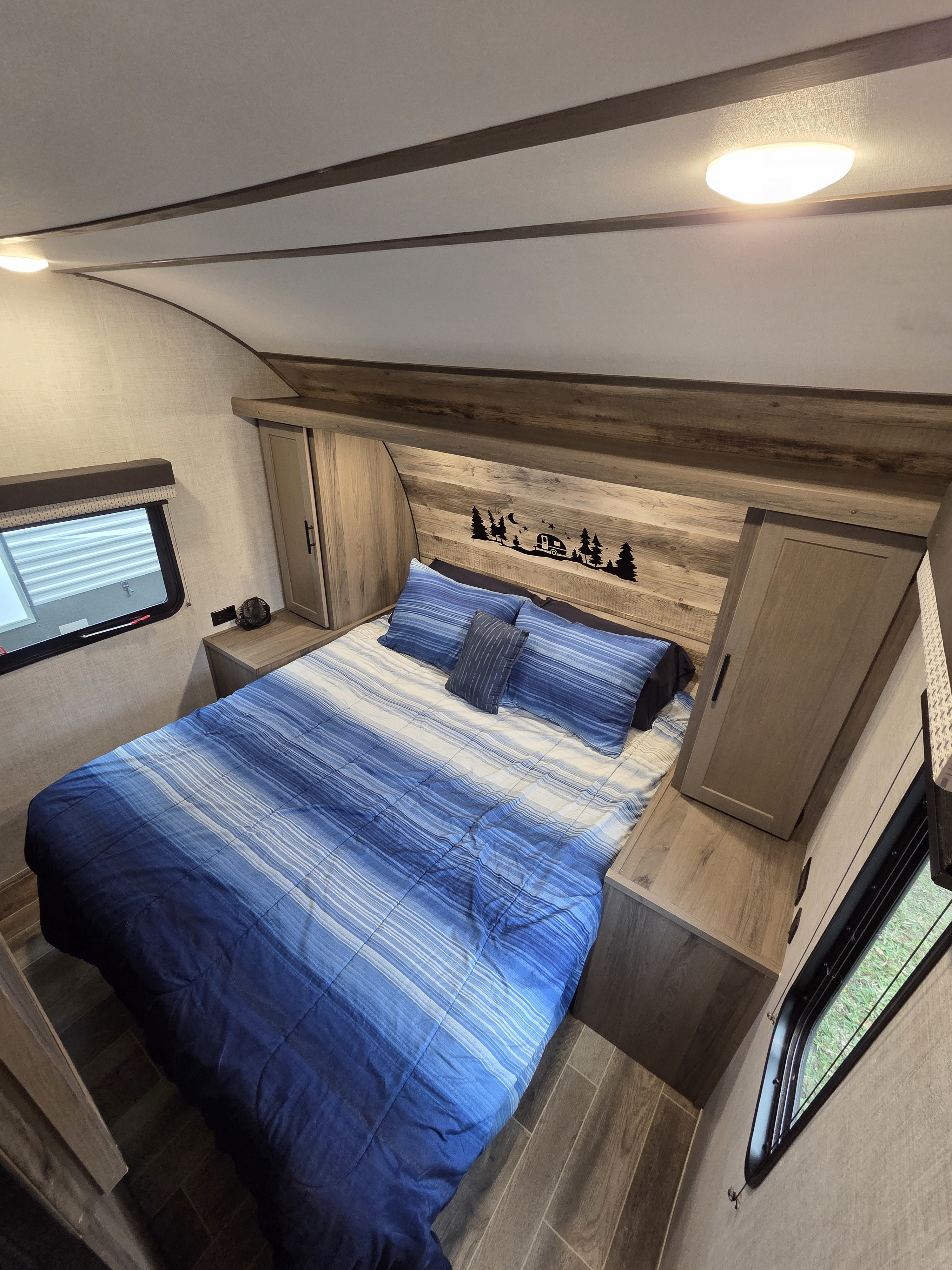 Cozy RV rental bedroom featuring a blue striped bed, wooden storage, overhead light, and a unique camper headboard.. Gulf Stream Kingsport 2022