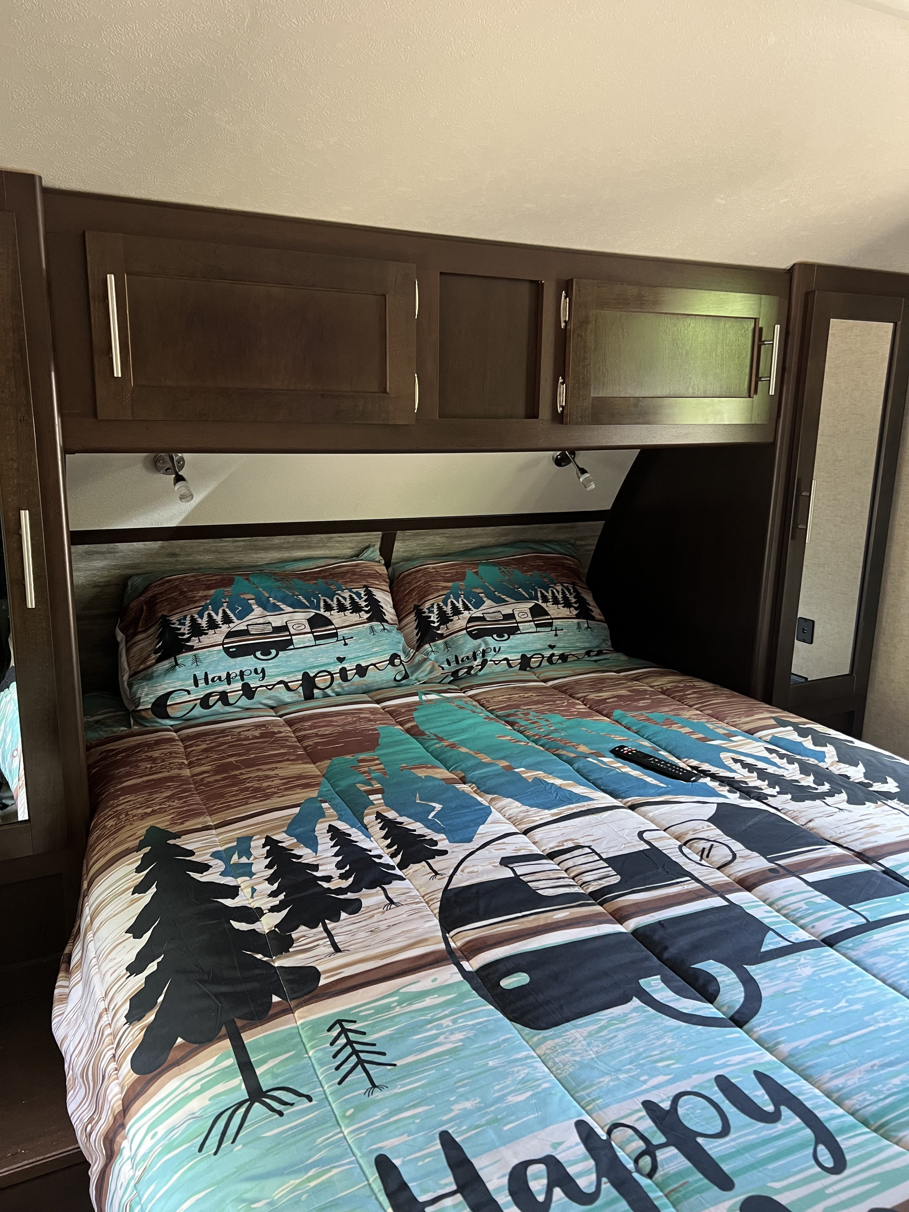 Cozy RV rental bedroom with "Happy Camping" themed bedding, dark wood cabinets, and reading lights. Perfect for travel adventures!. Forest River Cherokee 2018