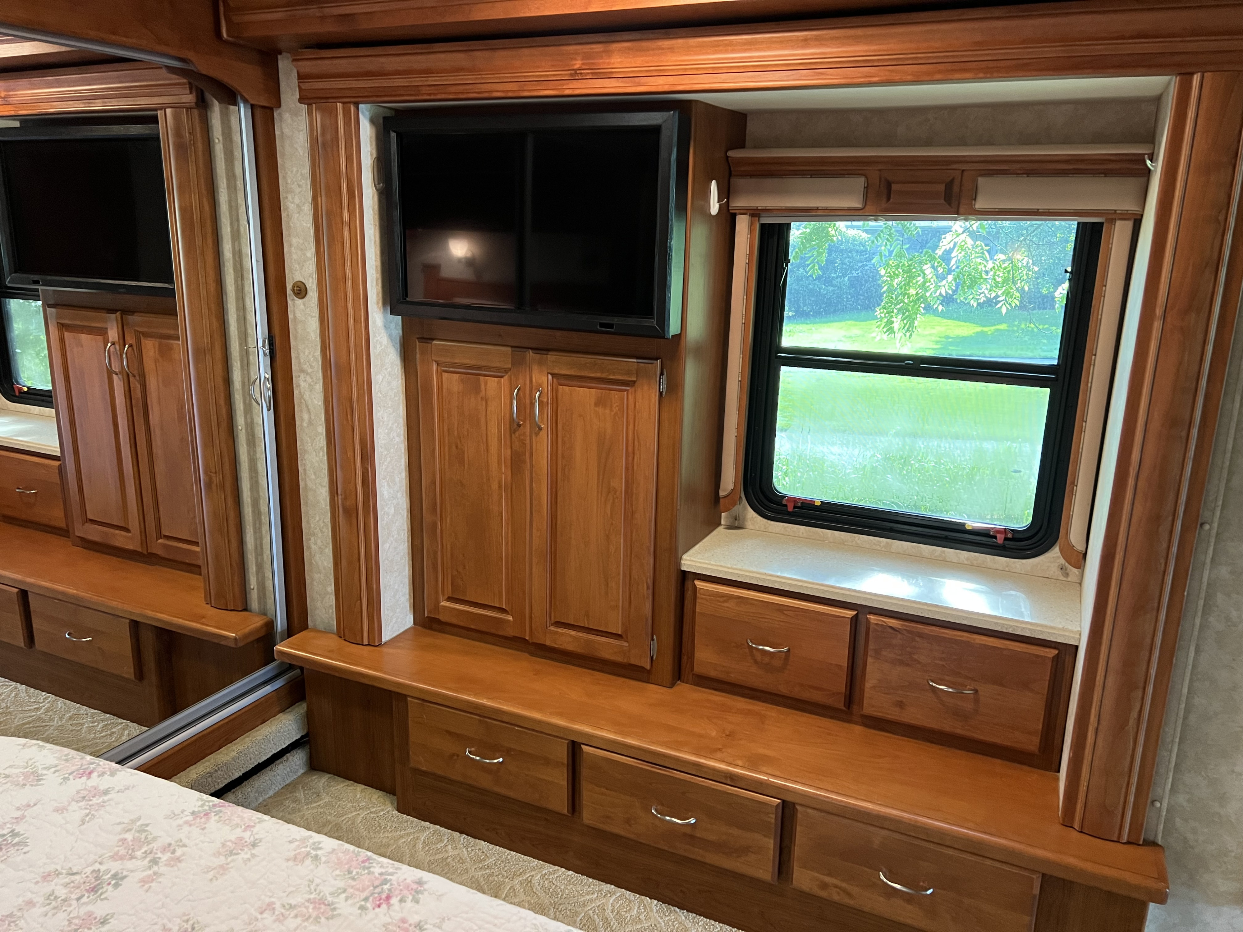 RV rental bedroom interior with a mounted TV, wooden storage cabinets, drawers, and a window view to nature.. Holiday Rambler Endeavor 2007