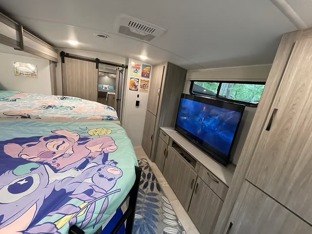 This RV rental interior features Lilo & Stitch bunk beds, an entertainment unit with a TV, and wood-look cabinetry.. Keystone RV Passport GT Ultra Lite 2024