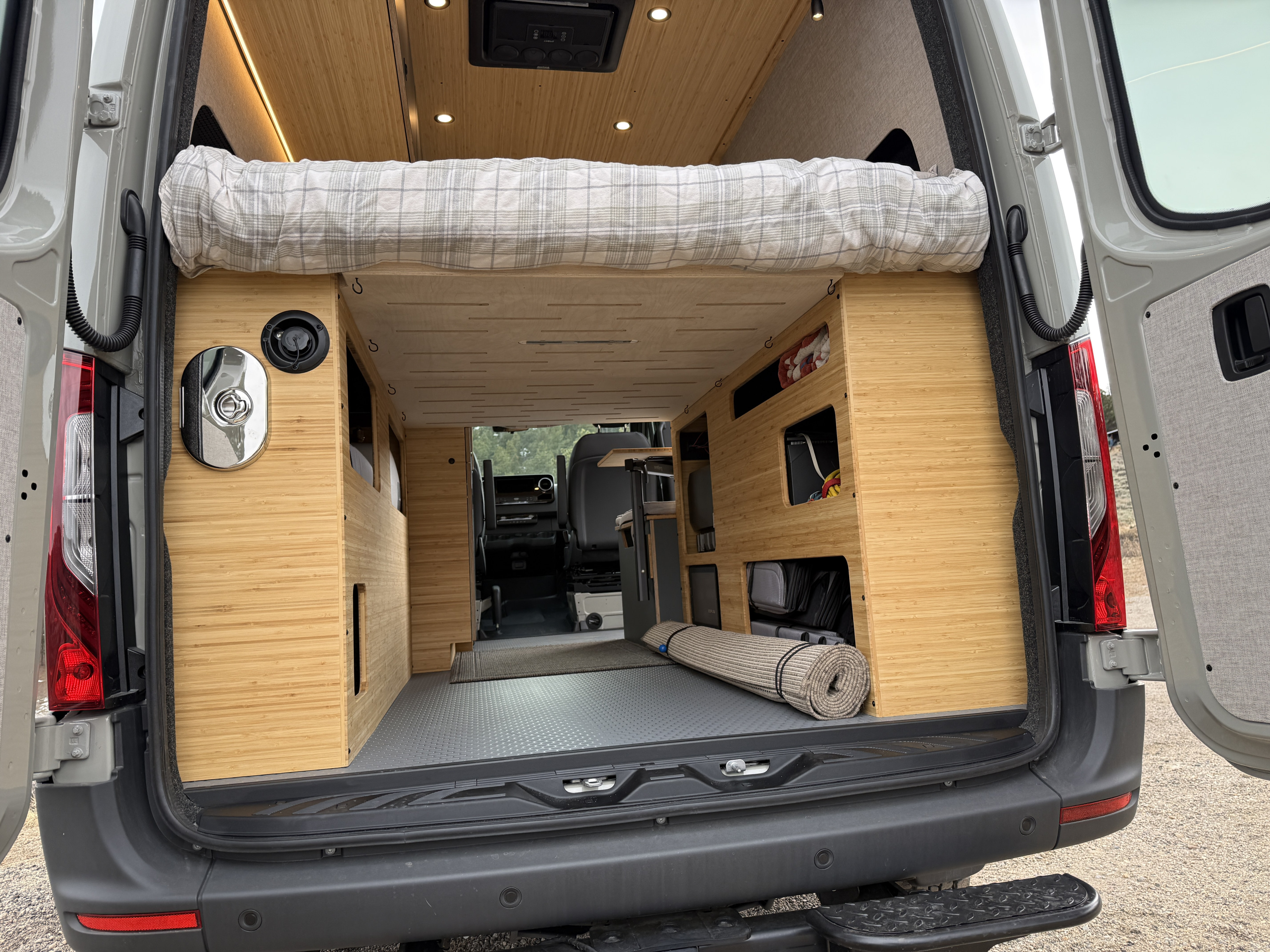 Back view of a modern rv rental camper van interior, showcasing a cozy bed above bamboo storage units & practical floor.. Mercedes-Benz Sprinter 2026