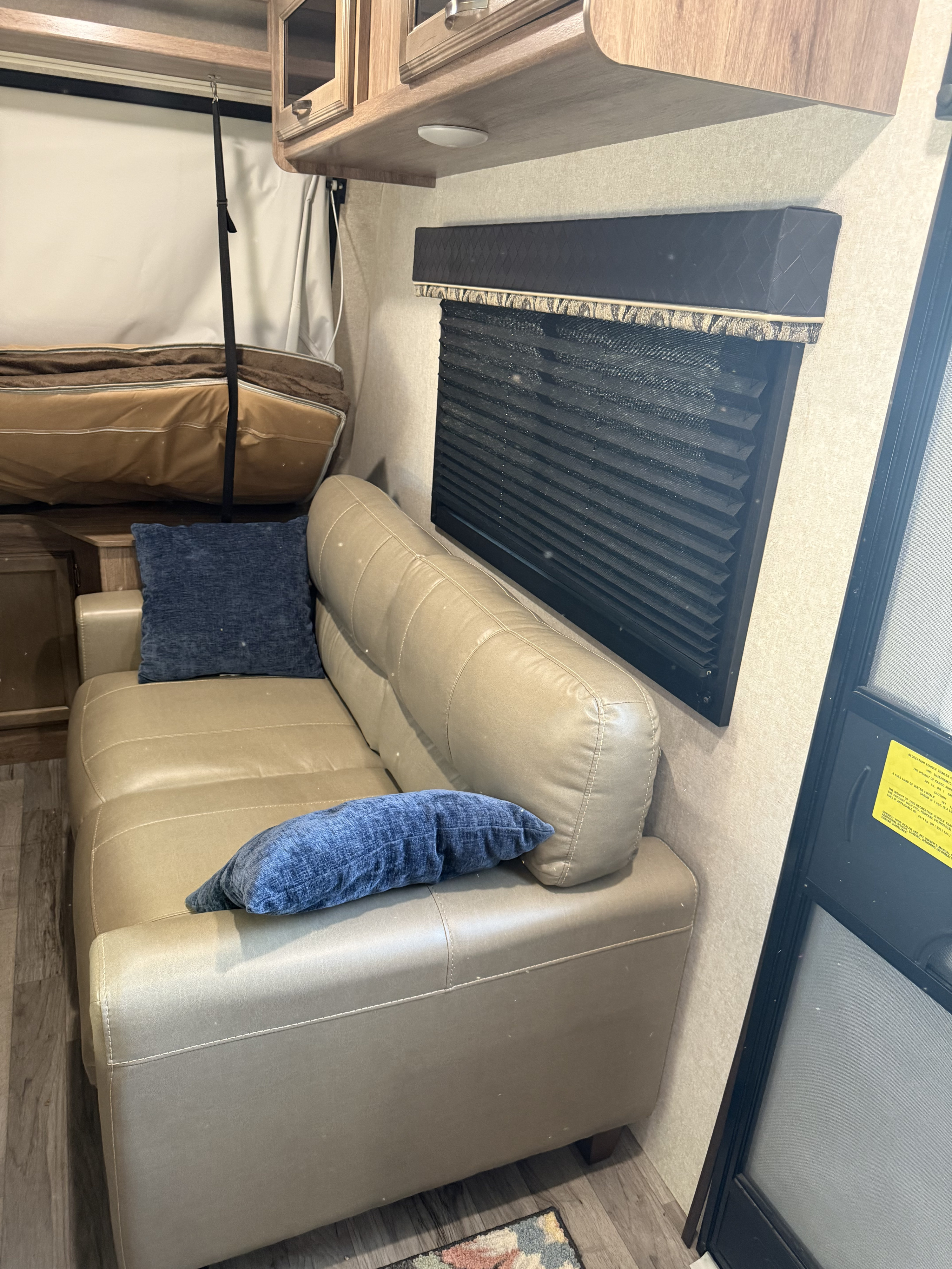 Cozy RV rental interior with a tan sofa, blue pillows, window blinds, and bunk bed. Perfect for a road trip!. Jayco Jay Feather 2020