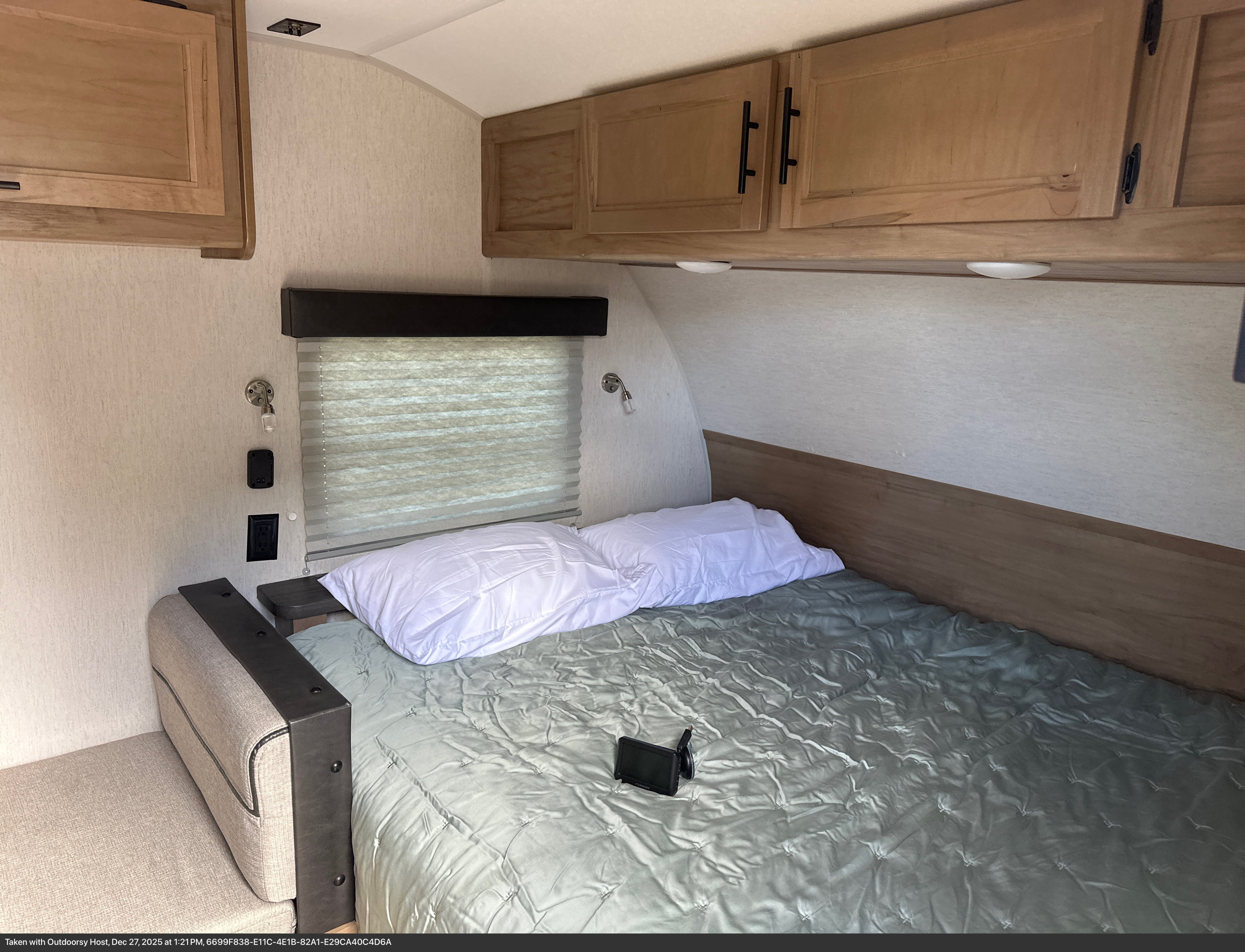 Cozy RV rental bedroom featuring a bed with green comforter, white pillows, overhead cabinets, and window blinds.. Forest River Cherokee Wolf Pup 2023