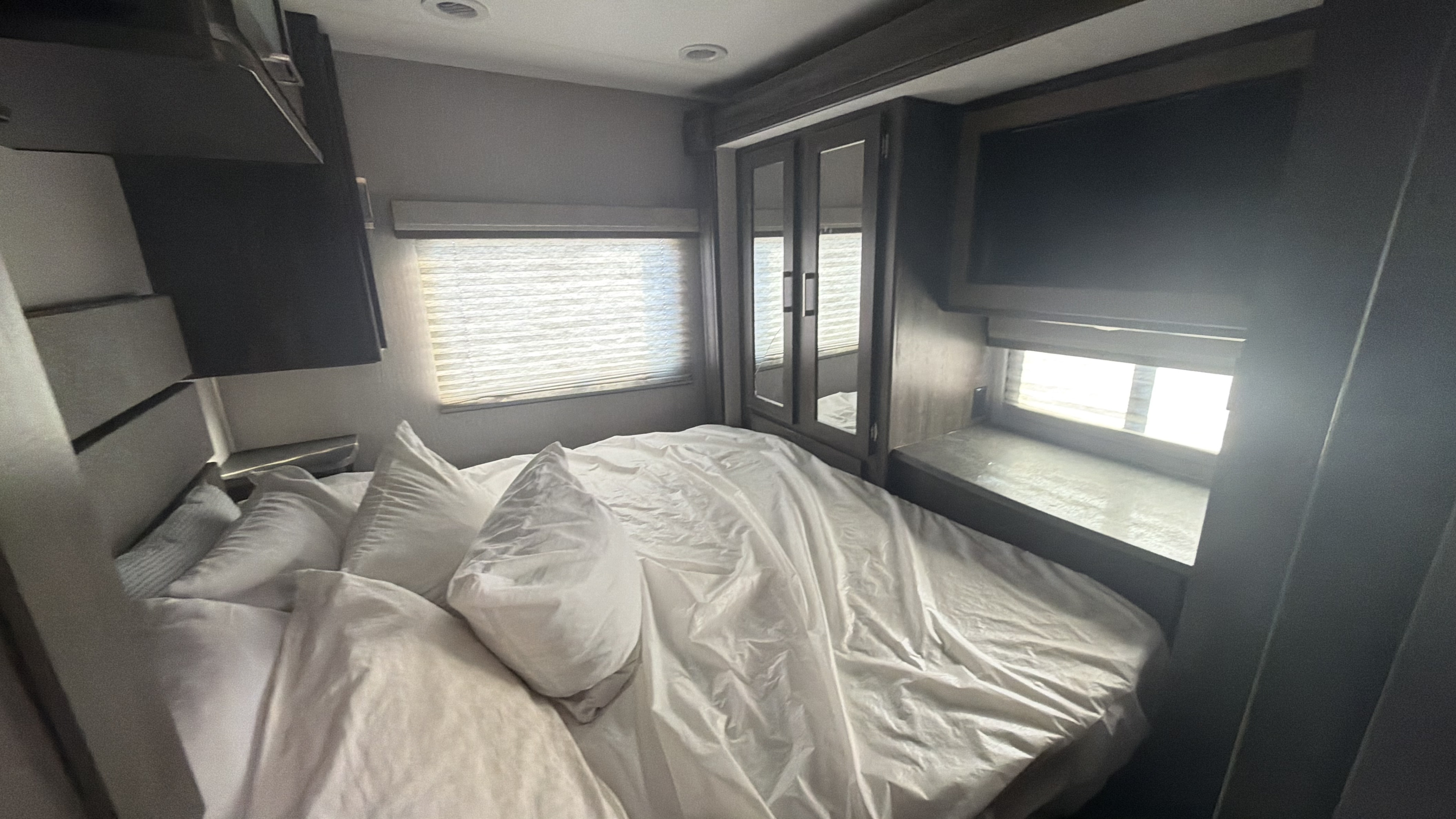 Explore this RV rental's modern bedroom: a comfortable bed with white linens, large windows, a TV, and mirrored cabinets.. Thor Four Winds 2023