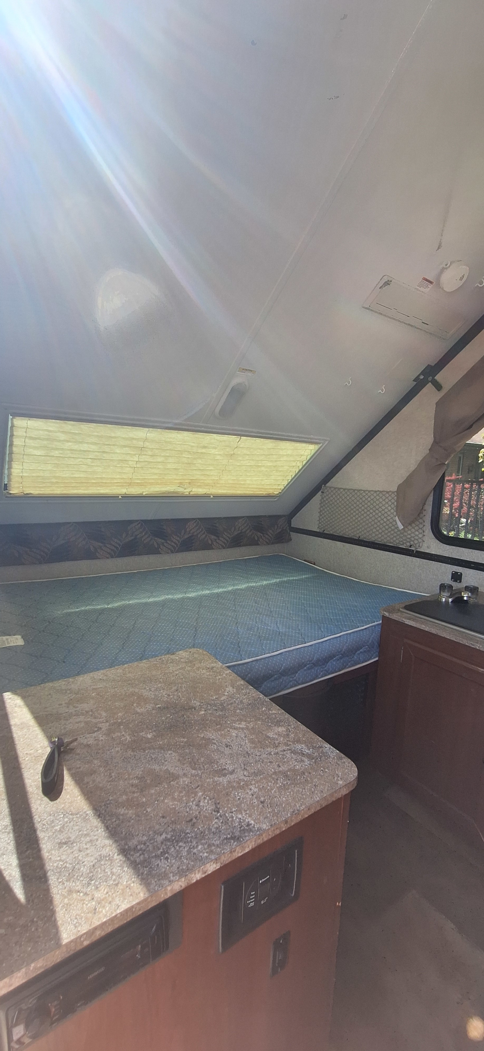 Cozy rv rental interior featuring a bed, kitchen counter, and window. Bright sunlight fills this compact camper.. Forest River Rockwood Premier 2016