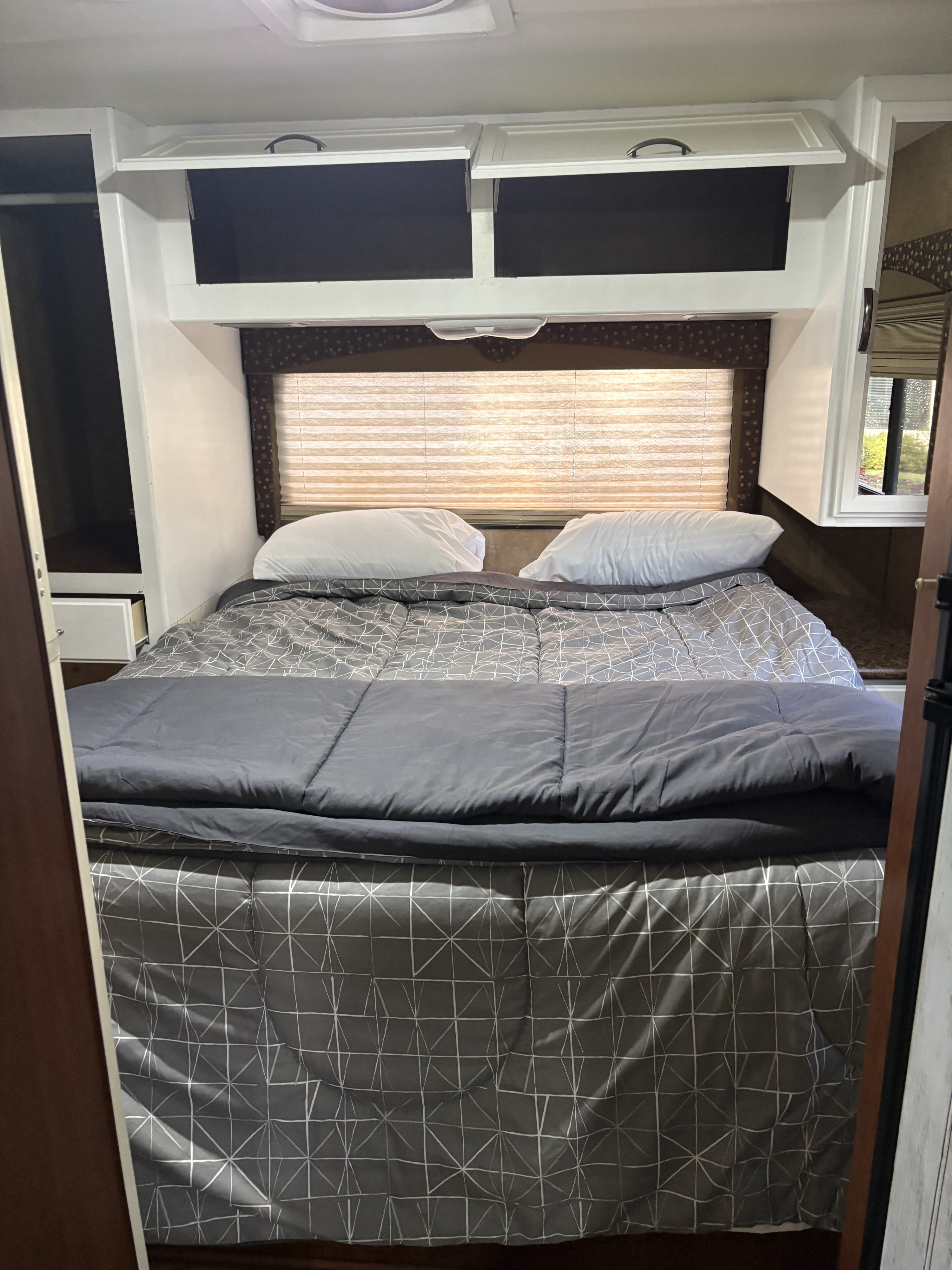 Comfortable RV rental bedroom with a made bed, overhead storage, and window with blinds for a cozy travel experience.. Thor Freedom Elite 2014