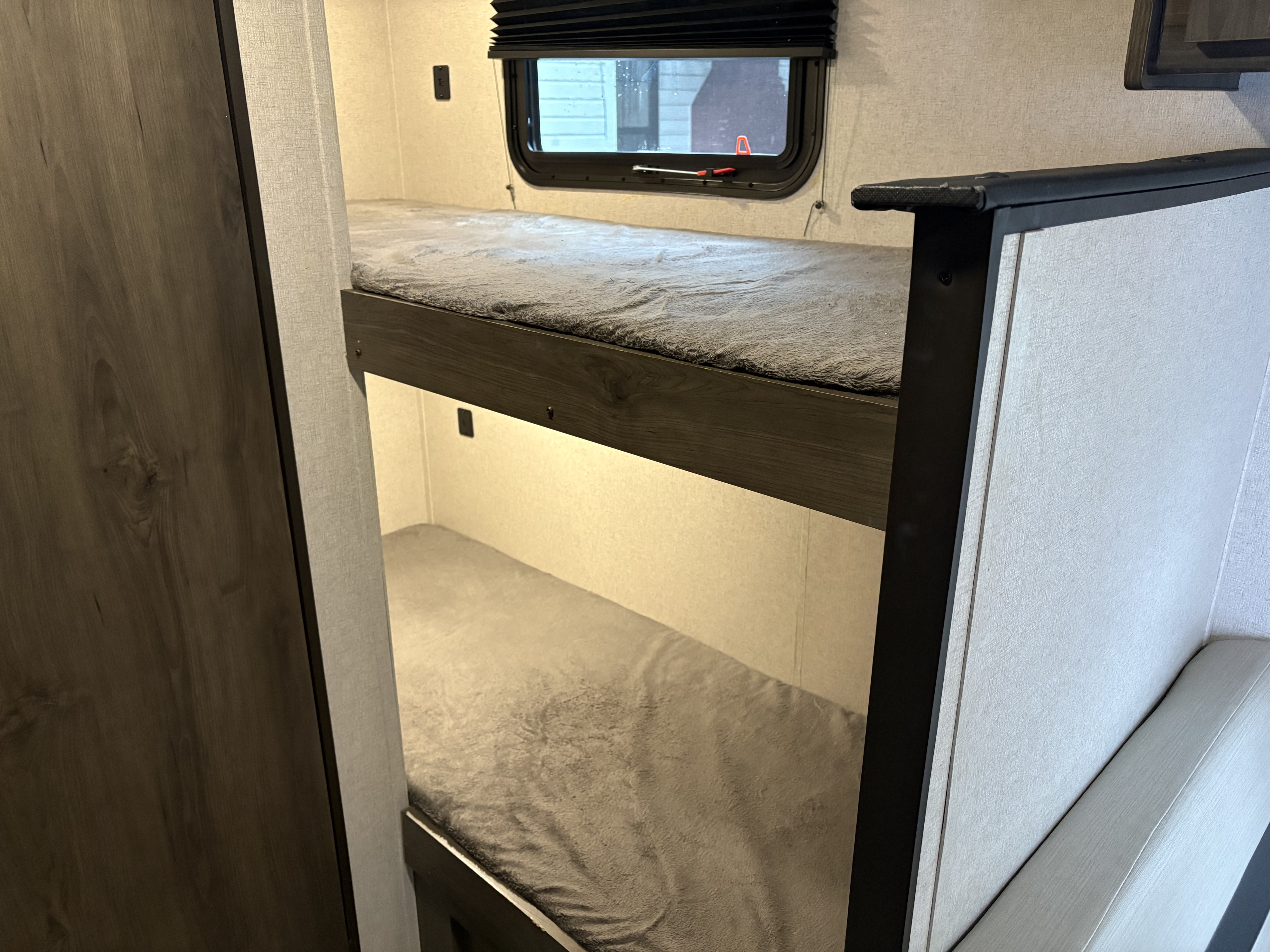 Cozy RV rental bunk beds with soft gray blankets, a window, and wood paneling, offering a comfortable camper interior.. Coachmen Clipper 2021