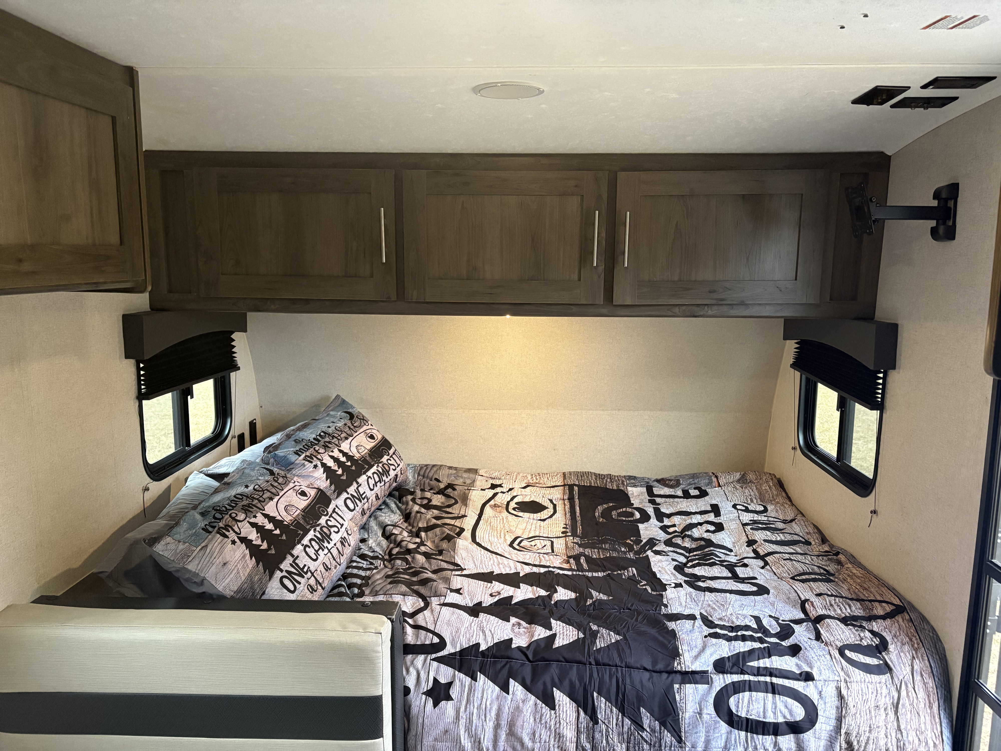 Cozy RV rental bedroom with camping-themed bedding, overhead cabinets, and windows, offering comfortable amenities.. Coachmen Clipper 2021
