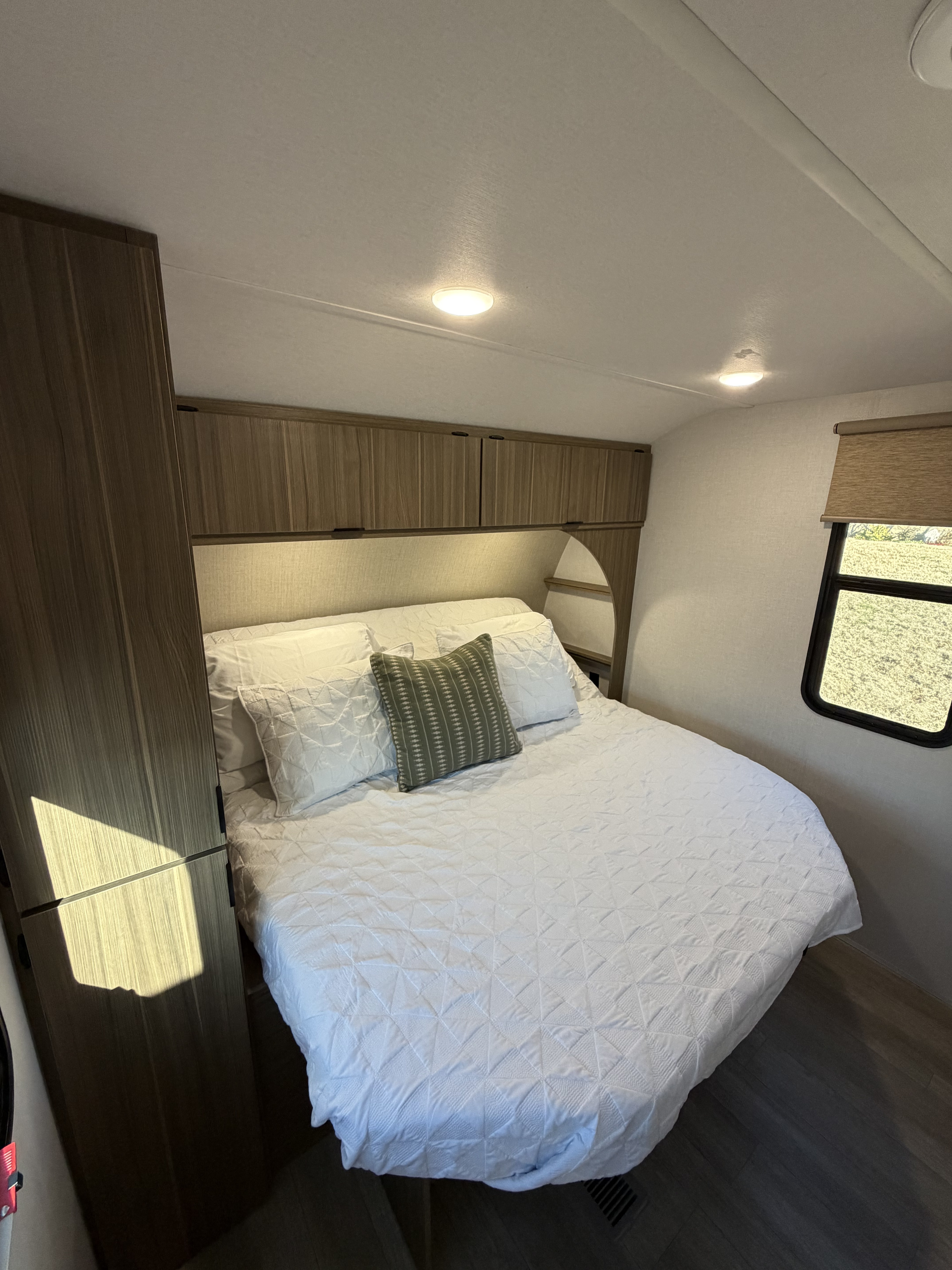 Step inside this clean RV rental bedroom, featuring a queen bed with white quilt, wood cabinets, and bright window.. Forest River Salem 29VBUD 2026