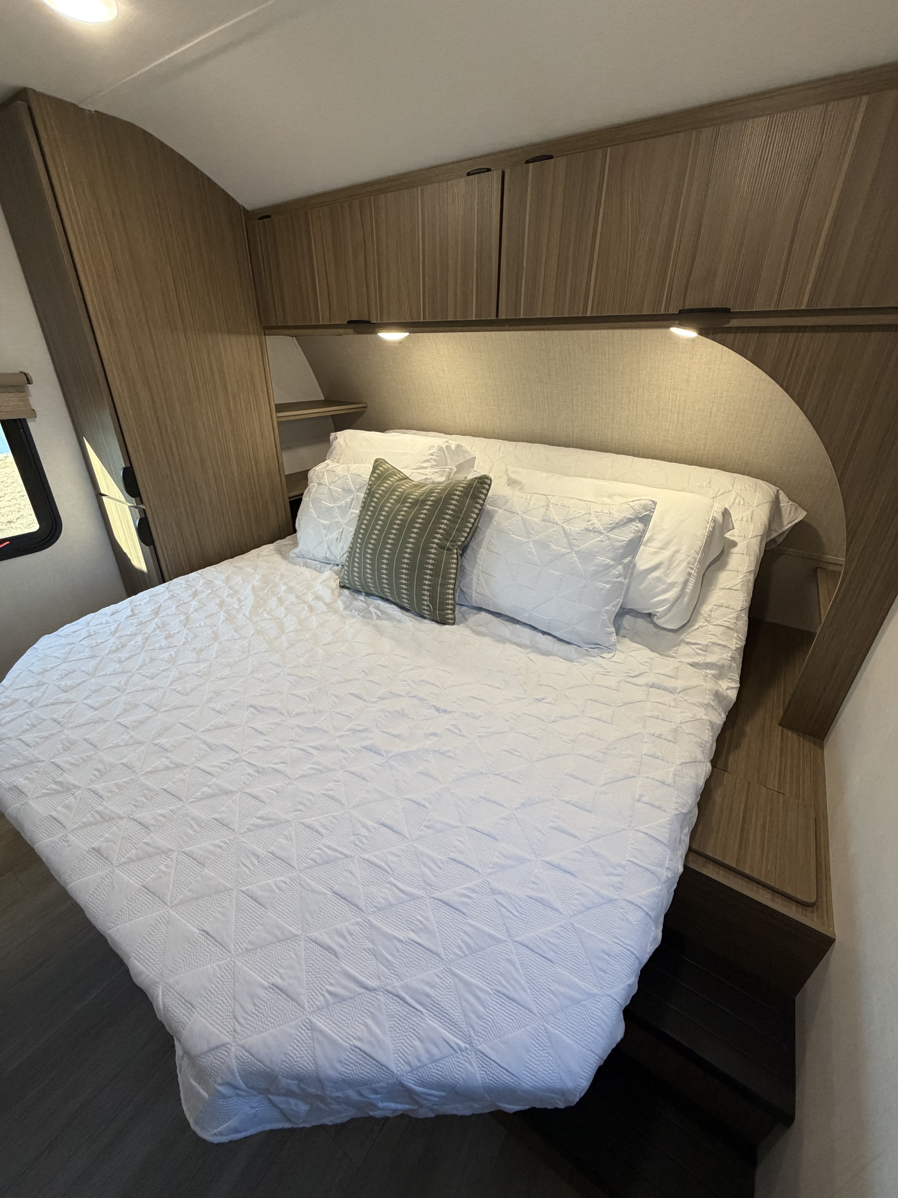 Modern rv rental bedroom featuring a large bed with a white quilted comforter & overhead wood cabinets.. Forest River Salem 29VBUD 2026