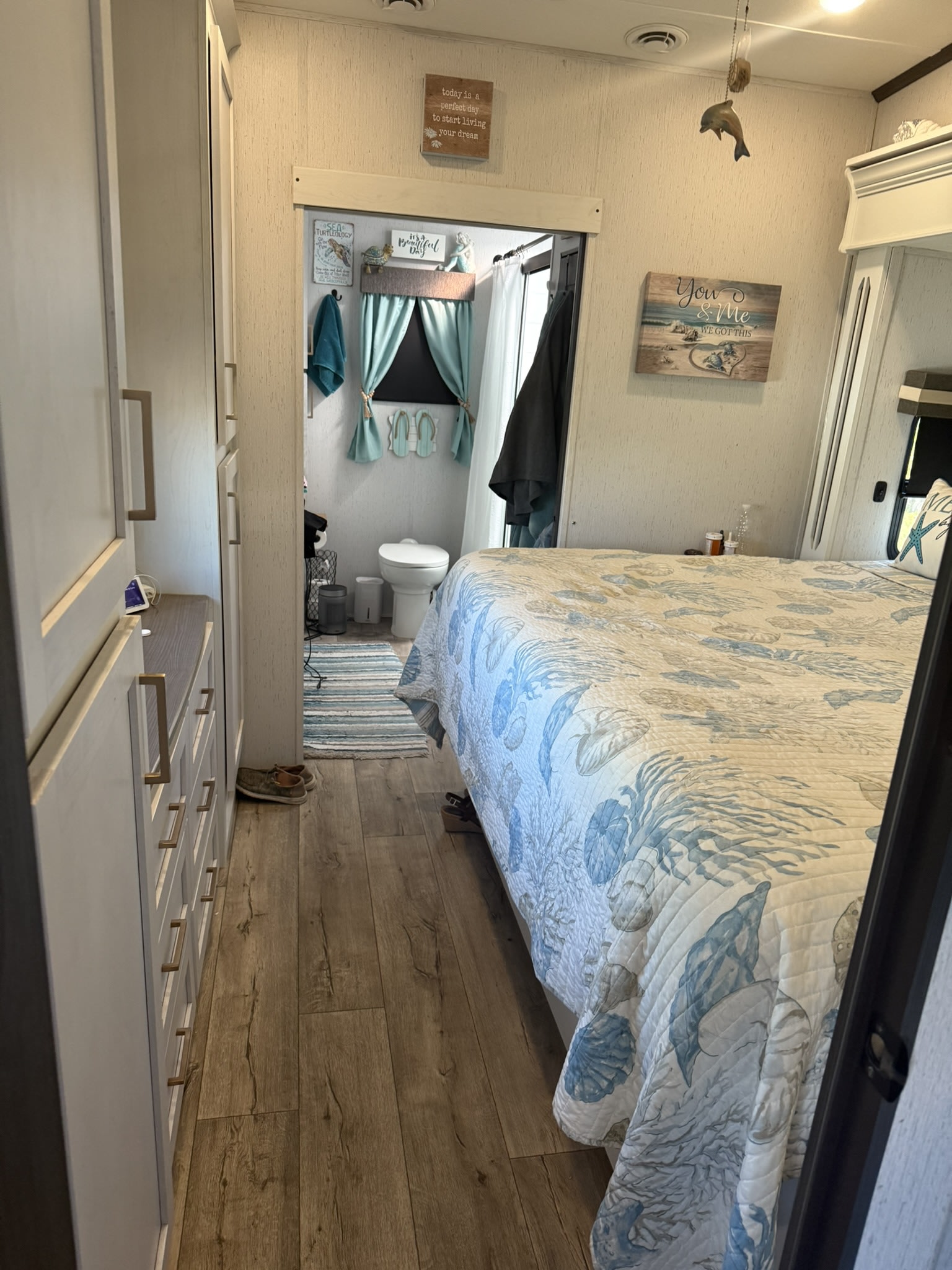 RV rental bedroom with light blue/white bedding & beach decor, showing a dresser & small bathroom. Cozy coastal retreat.. Astoria Platinum 2024