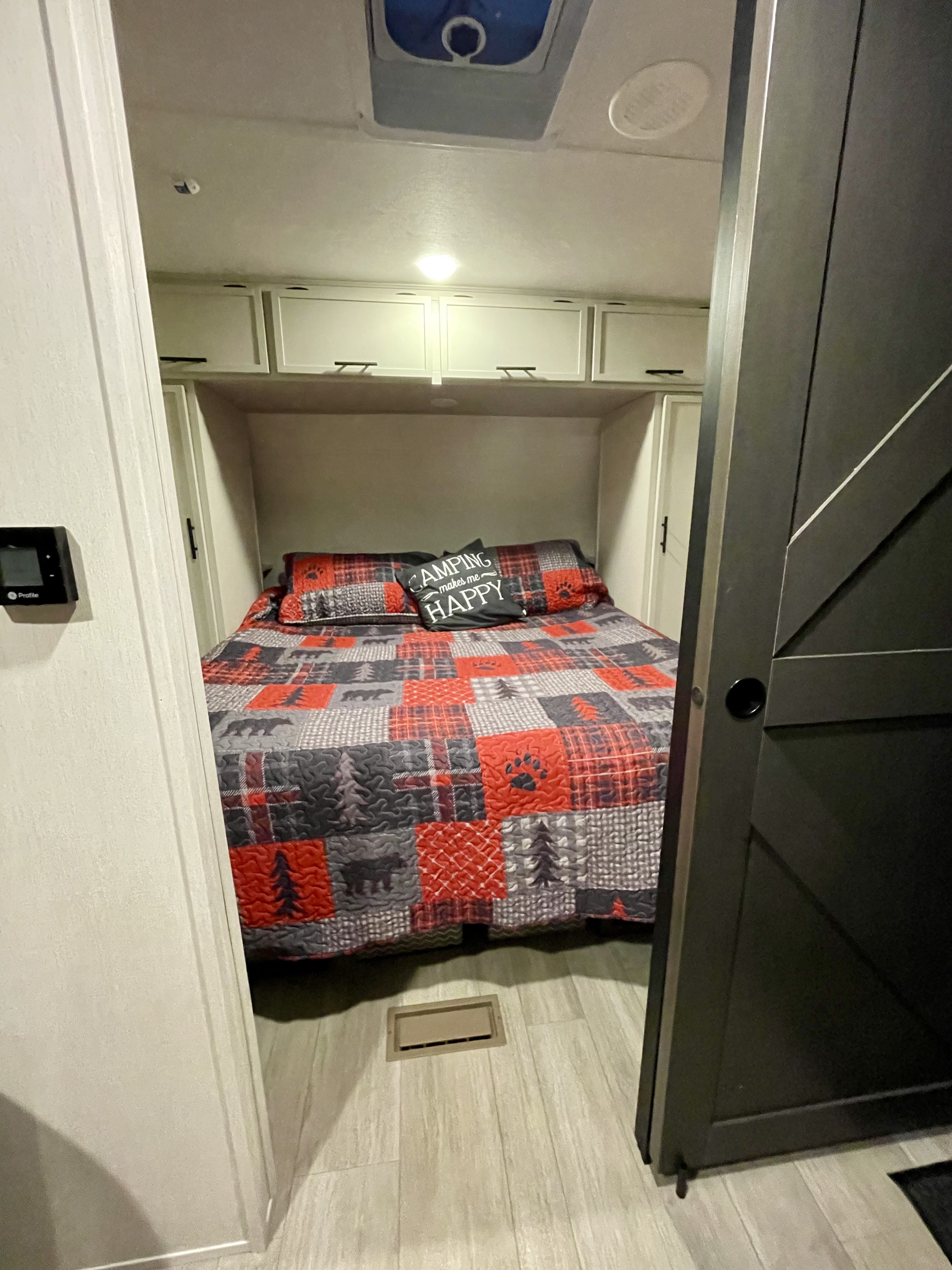 Cozy RV rental bedroom features a rustic camping quilt, overhead cabinets, a thermostat, and a sliding barn door.. Forest River Prime Time Avenger 2026