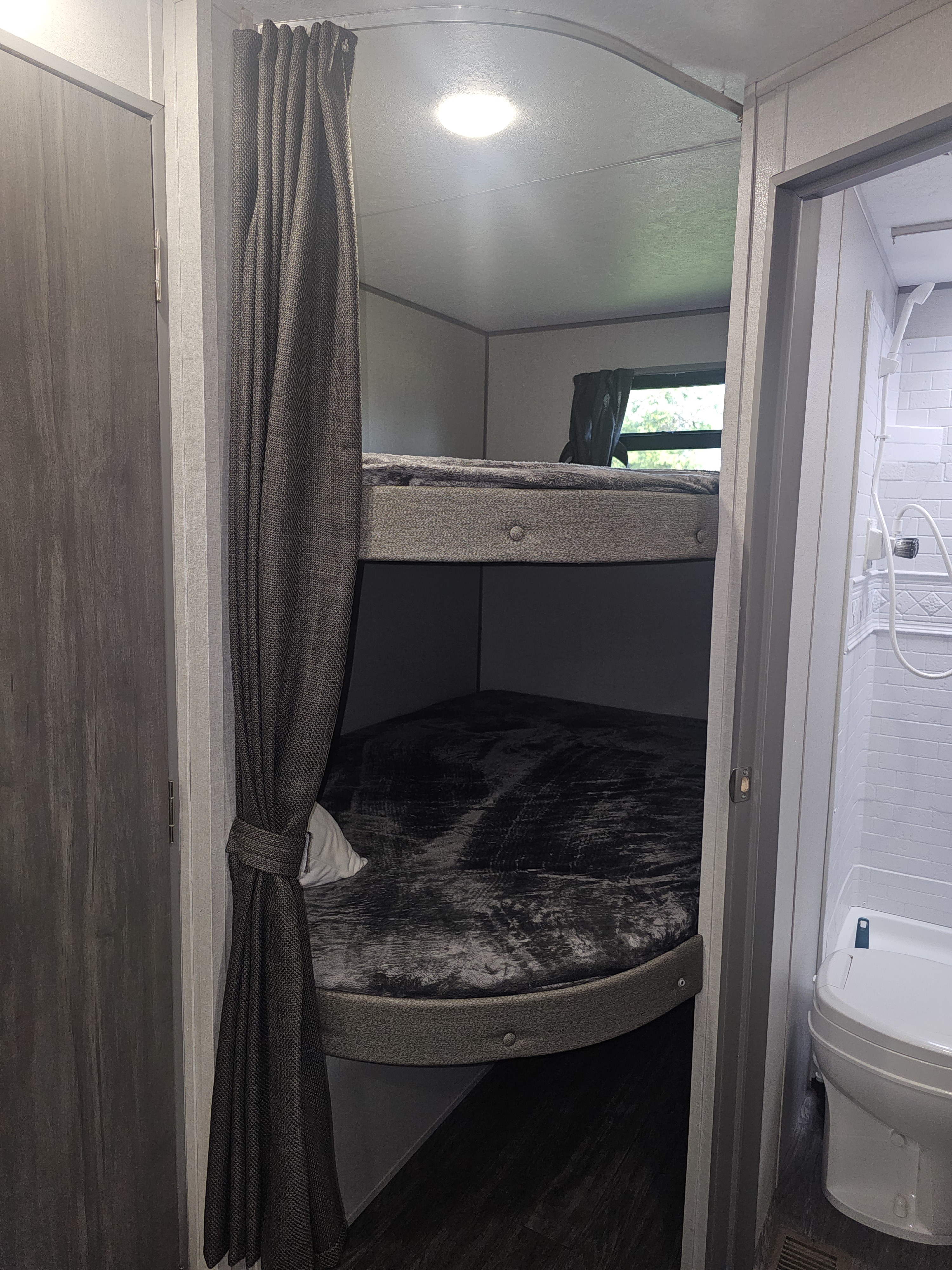 Inside an RV rental, showing a cozy bunk bed area with dark curtains and bedding, adjacent to a compact bathroom with a toilet and shower.. Forest River Aurora Aurora 2026
