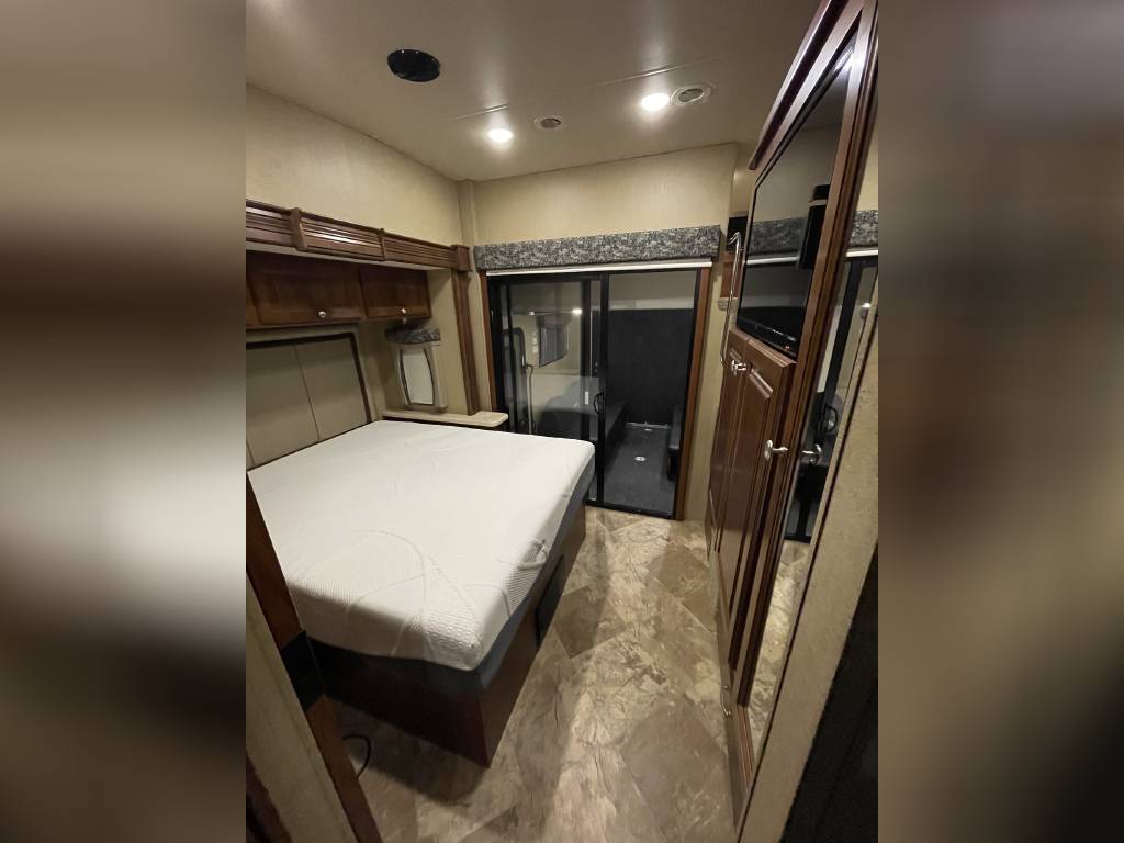 Comfortable RV rental bedroom with a large bed, wooden cabinets, and mirrored closet, offering cozy travel accommodation.. Thor Outlaw 2017