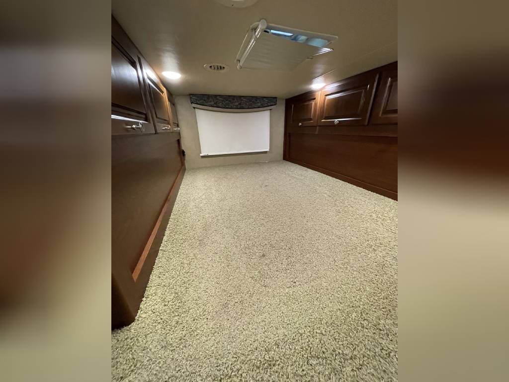 Inside an RV rental: a cozy bedroom or bunk space with light carpet, dark wood cabinetry, and a window blind.. Thor Outlaw 2017