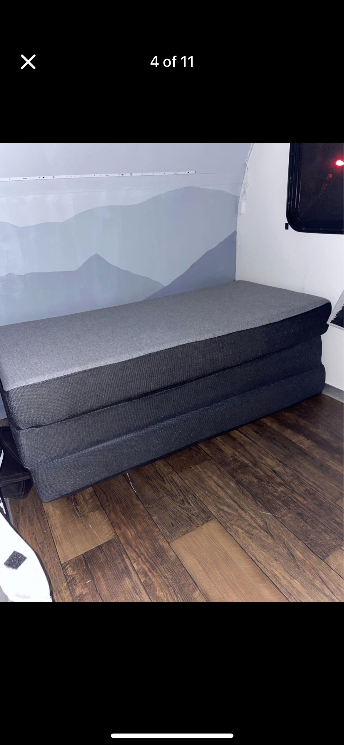 RV rental interior: A gray, three-section foldable mattress on a dark wood floor, set against a light mountain mural wall and strip lighting.. Rugged Mountain Custom RV Rustic Tear Drop Camper Koala 2022