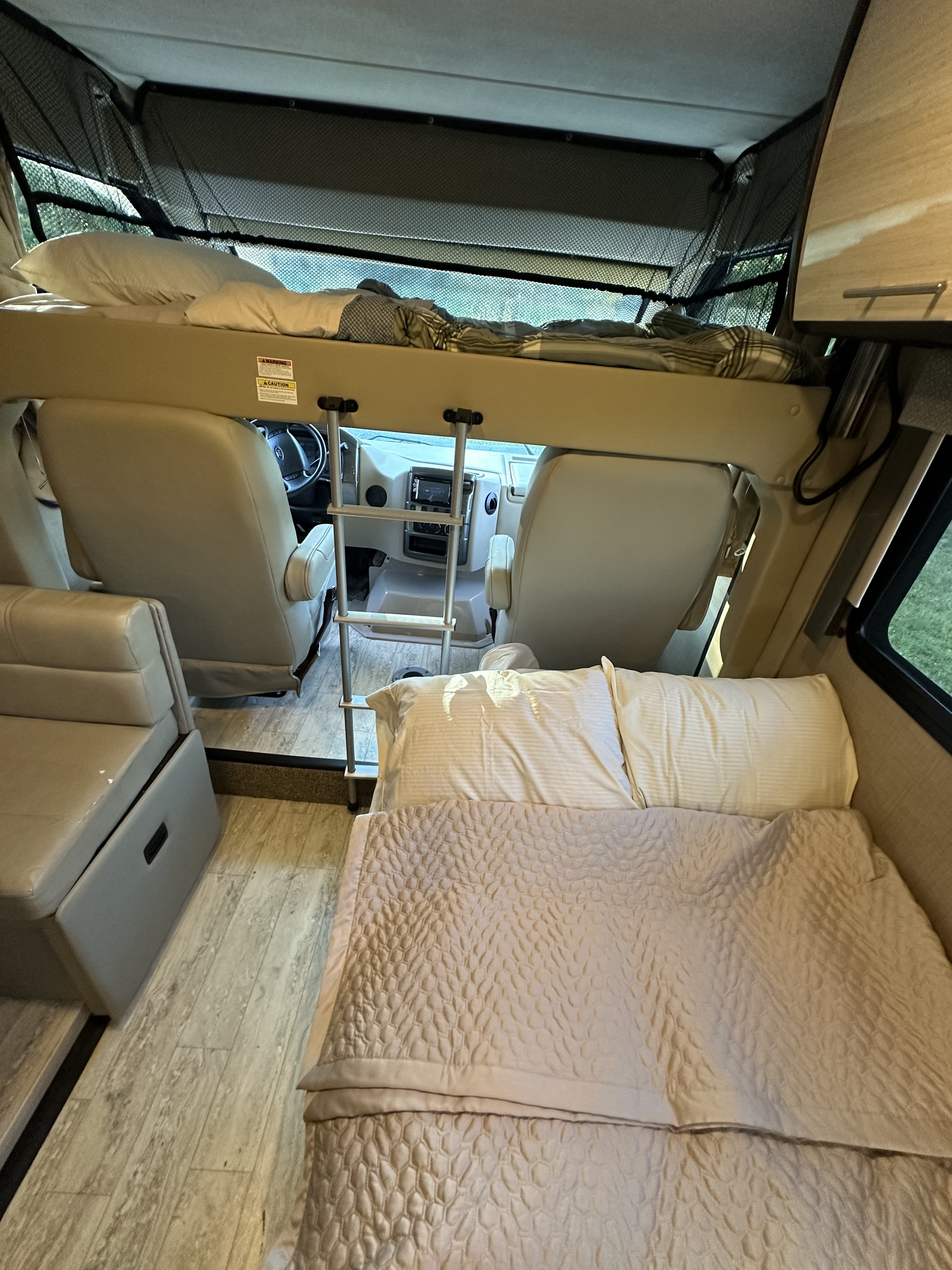 Inside an RV rental: a comfortable main bed, an overhead bunk bed with a safety net, and the cockpit area.. Thor Vegas 2018