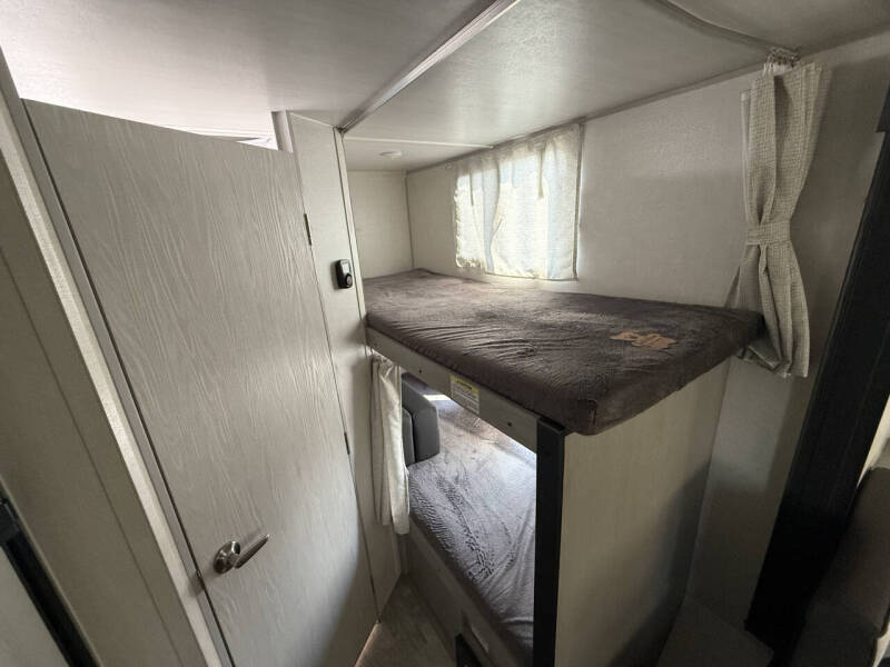 Inside this RV rental: functional bunk beds with a window & curtains, plus a door. Ideal for compact living on trips.. Forest River Ibex 2024