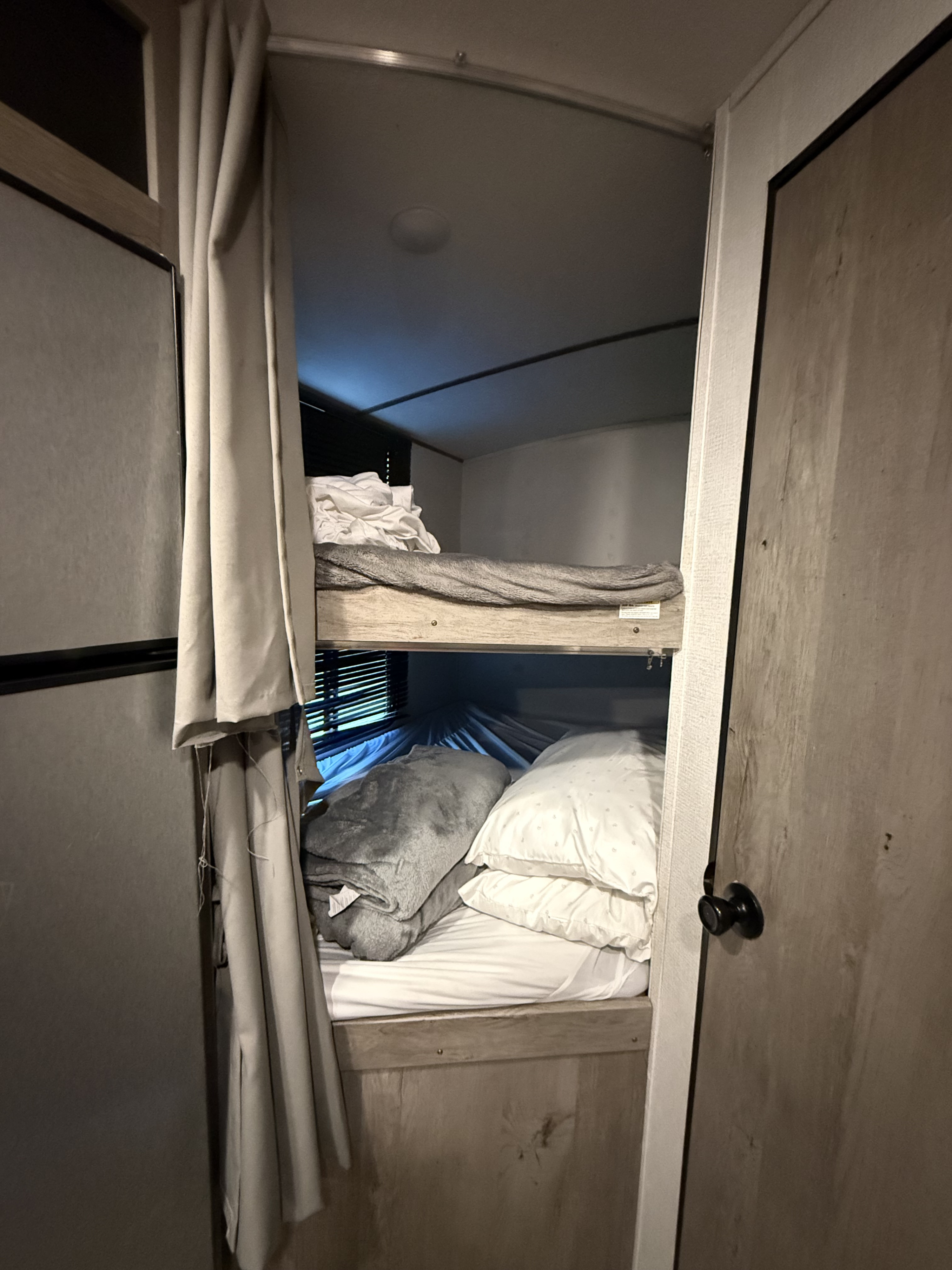 Two stacked bunk beds in an RV rental, furnished with white sheets, pillows, and gray blankets for a compact, cozy sleeping area.. Keystone RV Springdale 2021