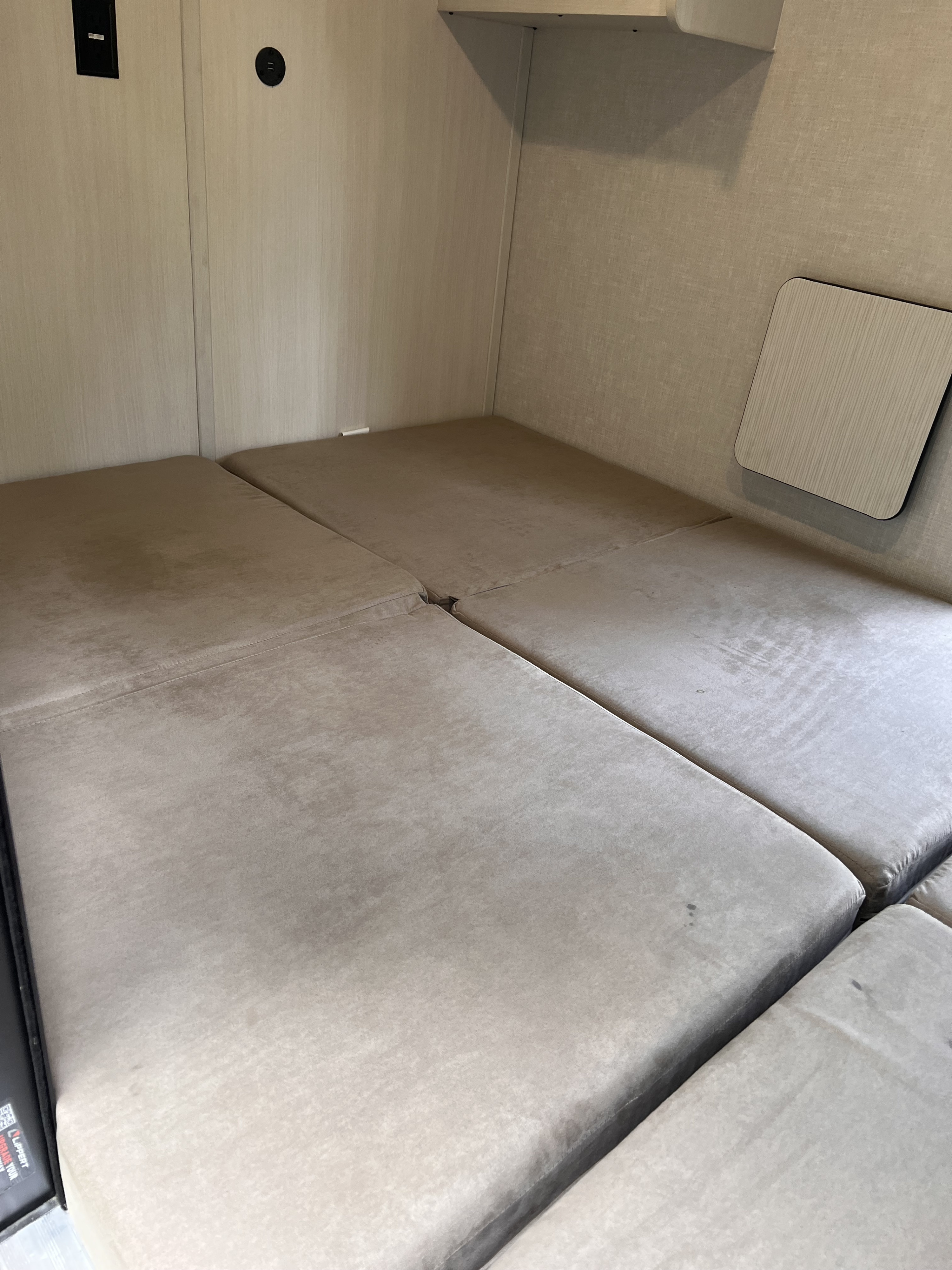 RV rental bed area with light-colored upholstered cushions, wall paneling, and charging ports. A small table is on the right.. Forest River NoBo 10.7 2024
